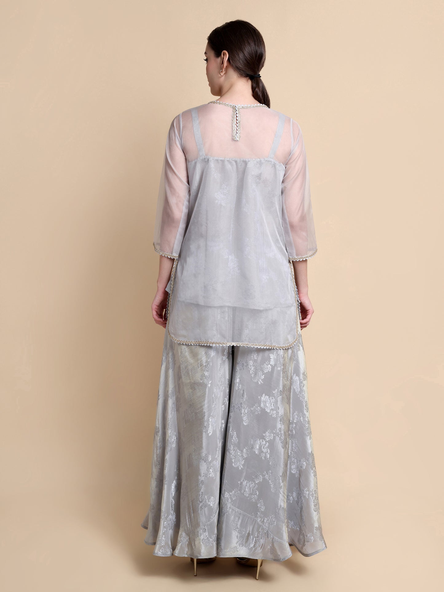 Woman wearing a light gray traditional outfit with a sheer top on a beige background