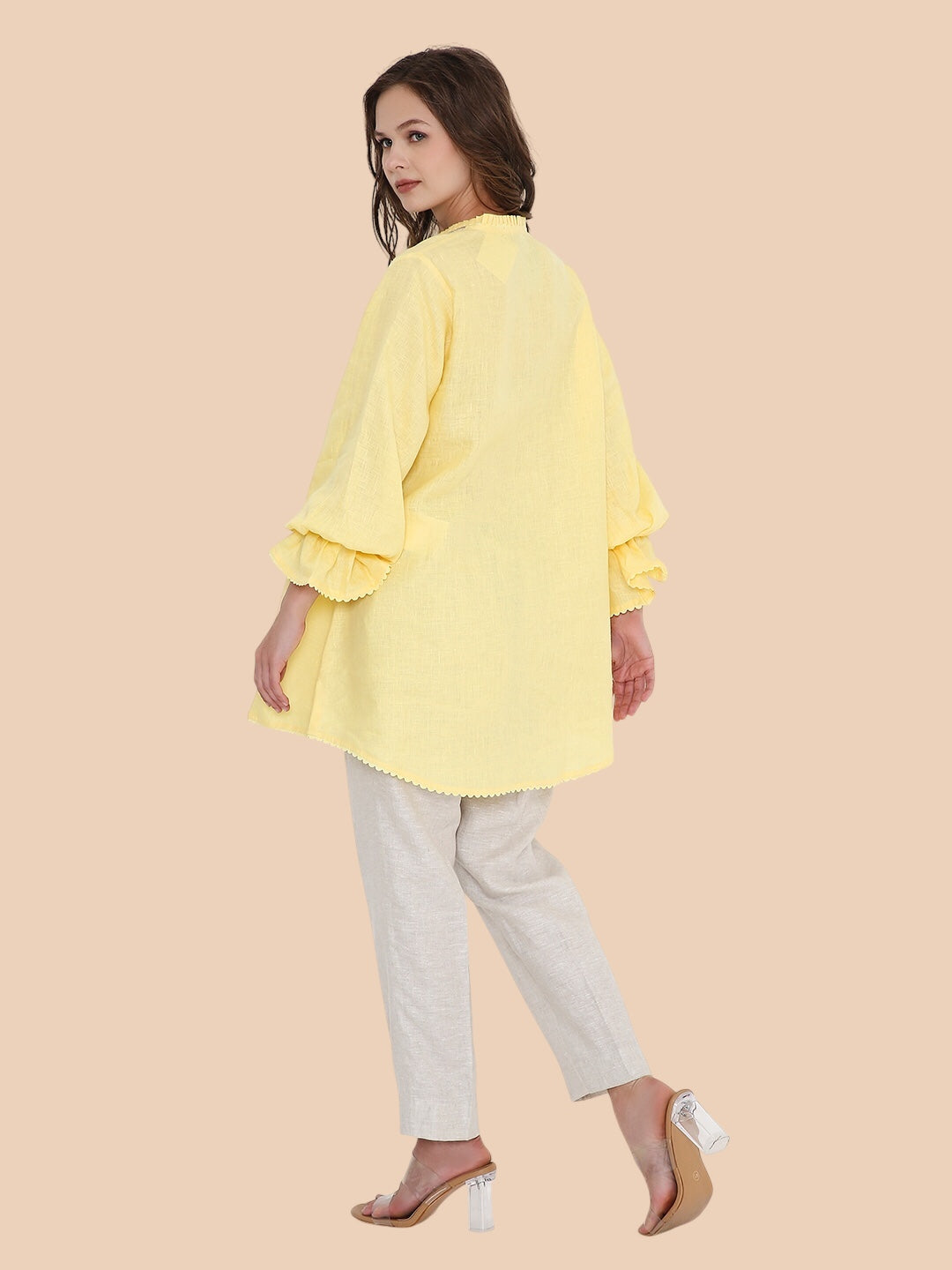 Woman wearing a yellow blouse and light gray pants on a beige background