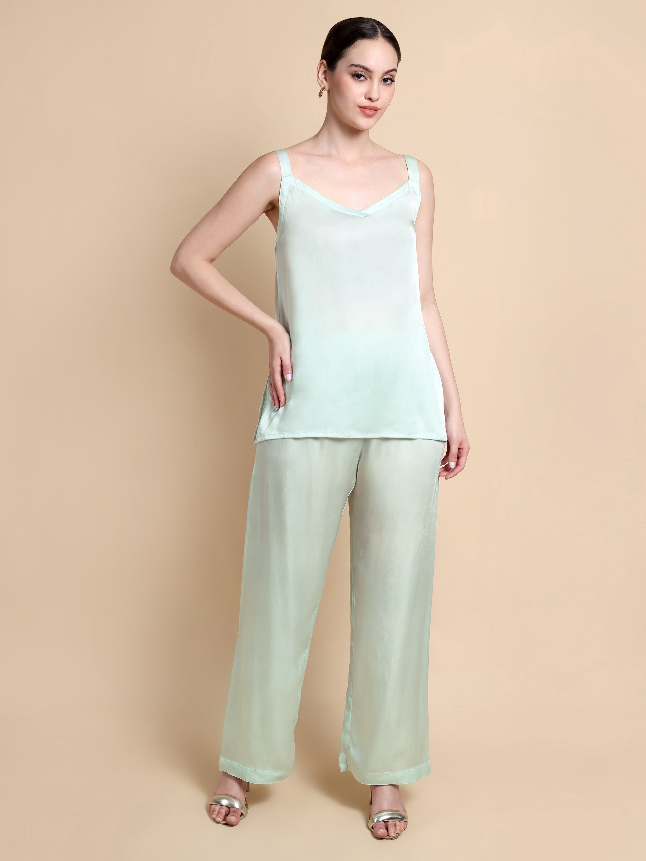 Woman wearing a light green sleeveless top and pants on a beige background