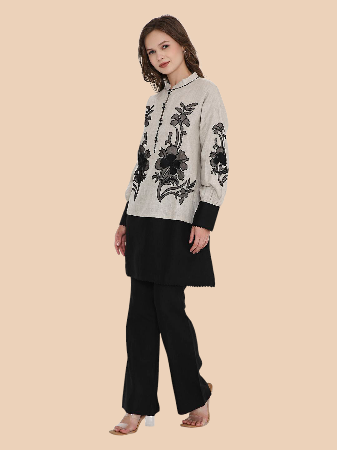 Woman wearing a black and white floral embroidered top with black pants on a beige background