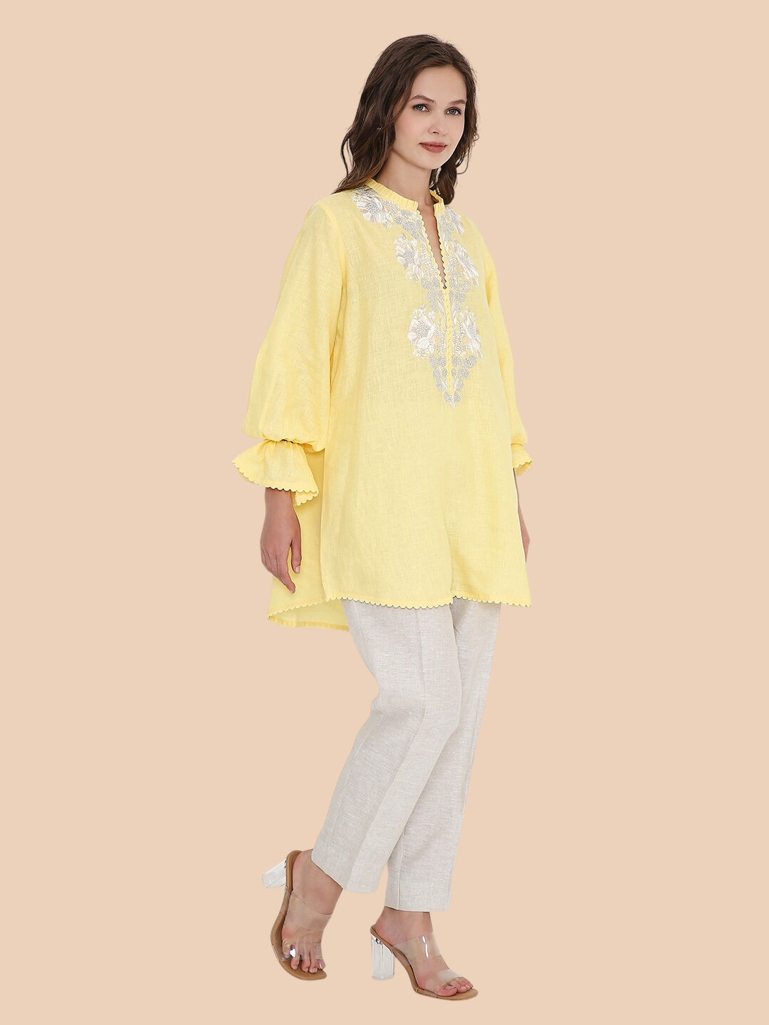 Woman wearing a yellow embroidered top and white pants on a beige background