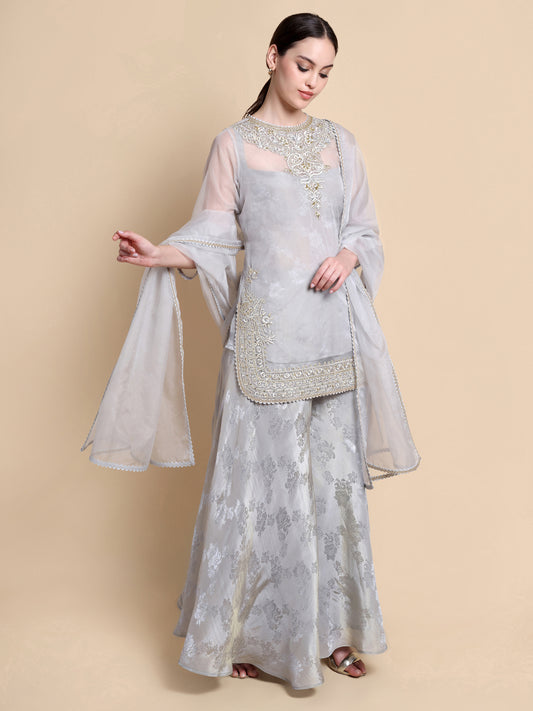 Woman wearing a light gray traditional outfit with floral patterns on a beige background