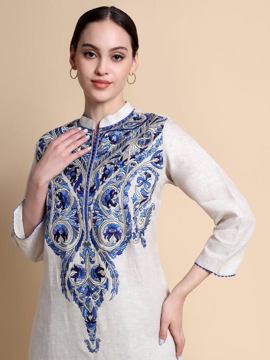 Woman wearing a white kurta with blue and purple floral embroidery on a beige background