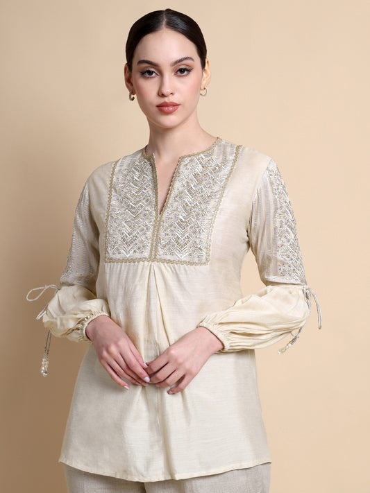 Woman wearing a cream-colored kurta with intricate lace detailing on a beige background