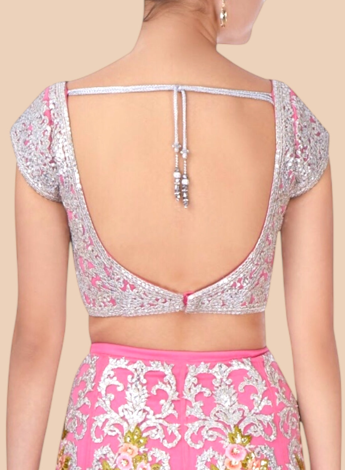 Back view of a person wearing a floral blouse with a pink and white patterned skirt on a beige background.