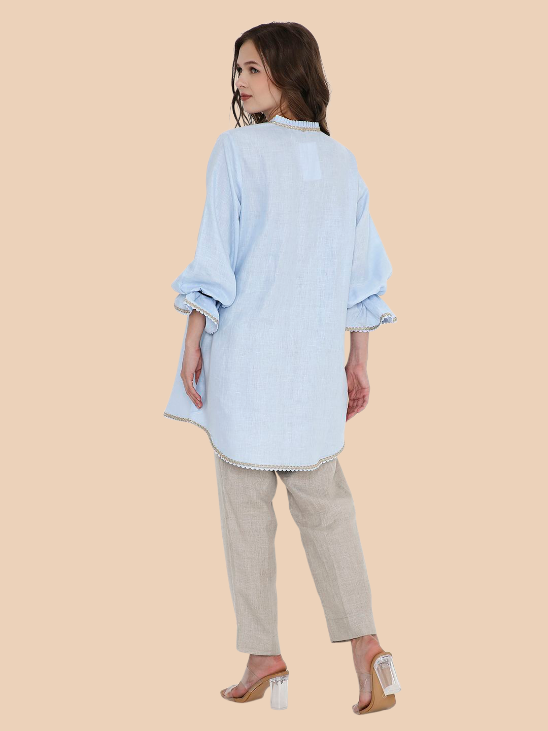 Woman wearing a light blue shirt and beige pants on a beige background