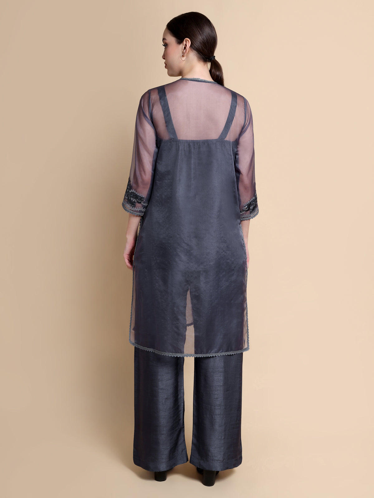 Woman wearing a dark gray dress with sheer sleeves on a beige background