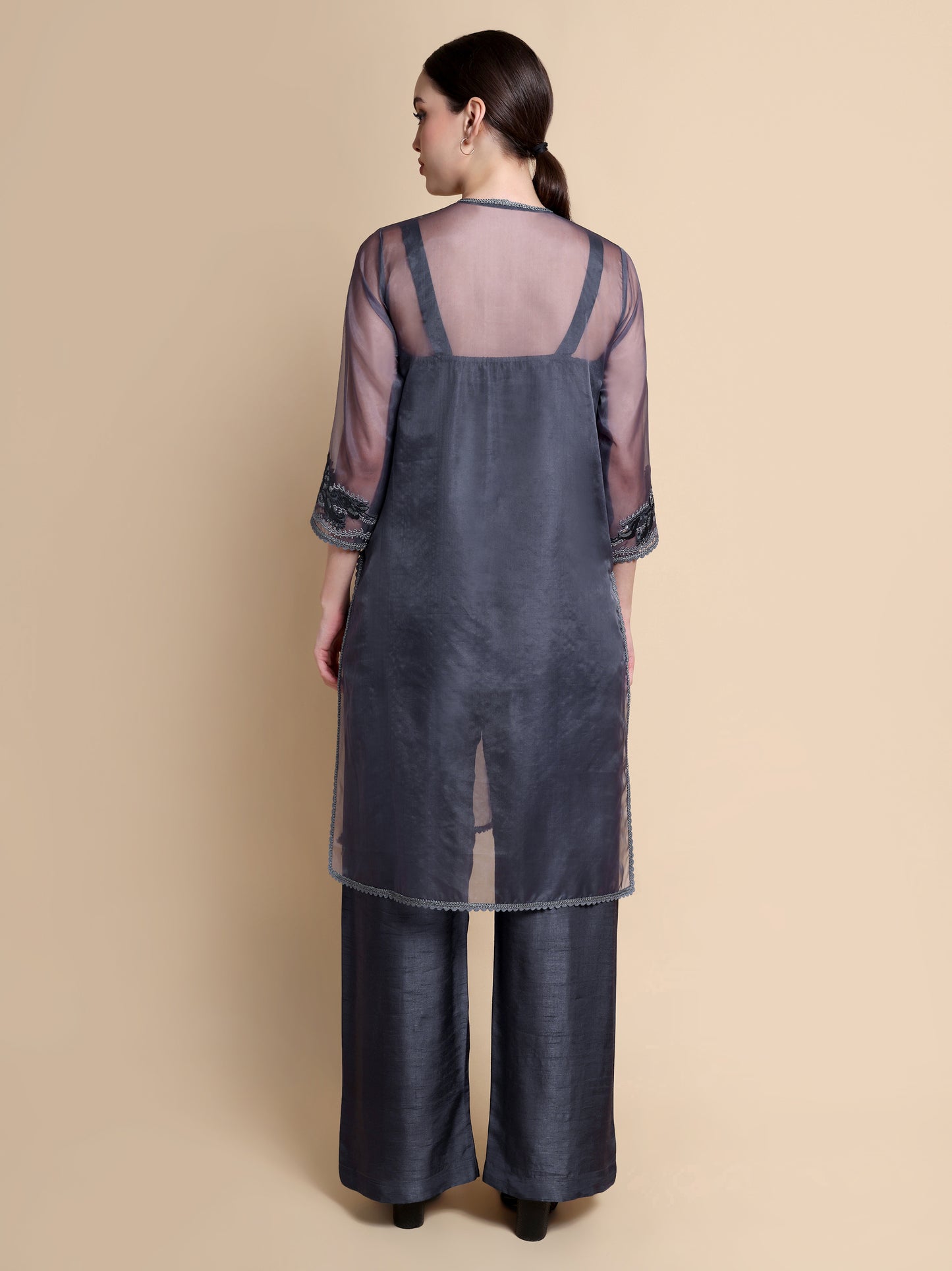 Woman wearing a dark gray dress with sheer sleeves on a beige background