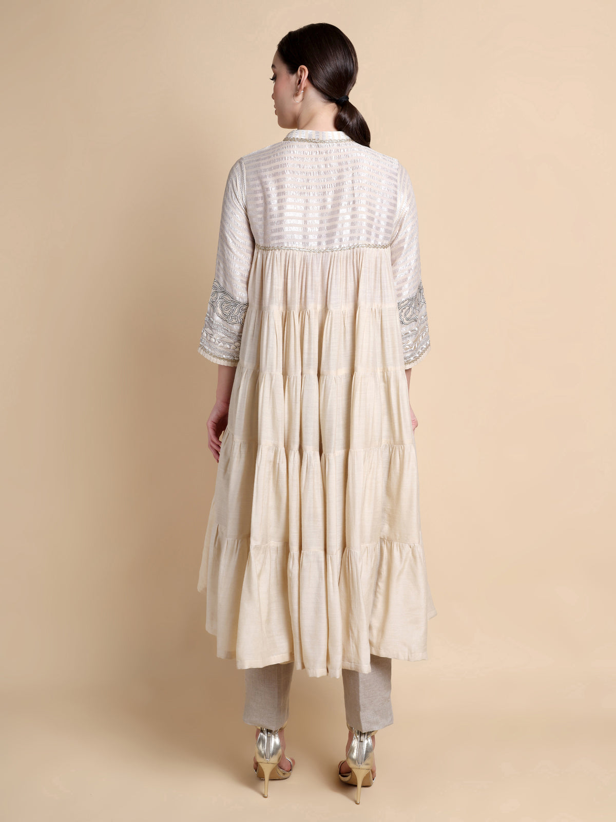 Woman wearing a cream-colored traditional outfit with intricate patterns on a beige background