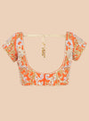 Orange embroidered blouse with gold and white details on a beige background
