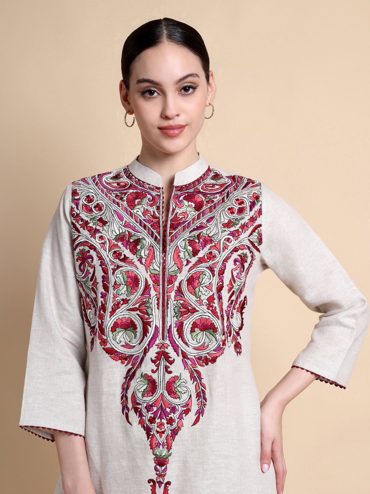 Woman wearing a white kurta with red and green embroidery on a beige background