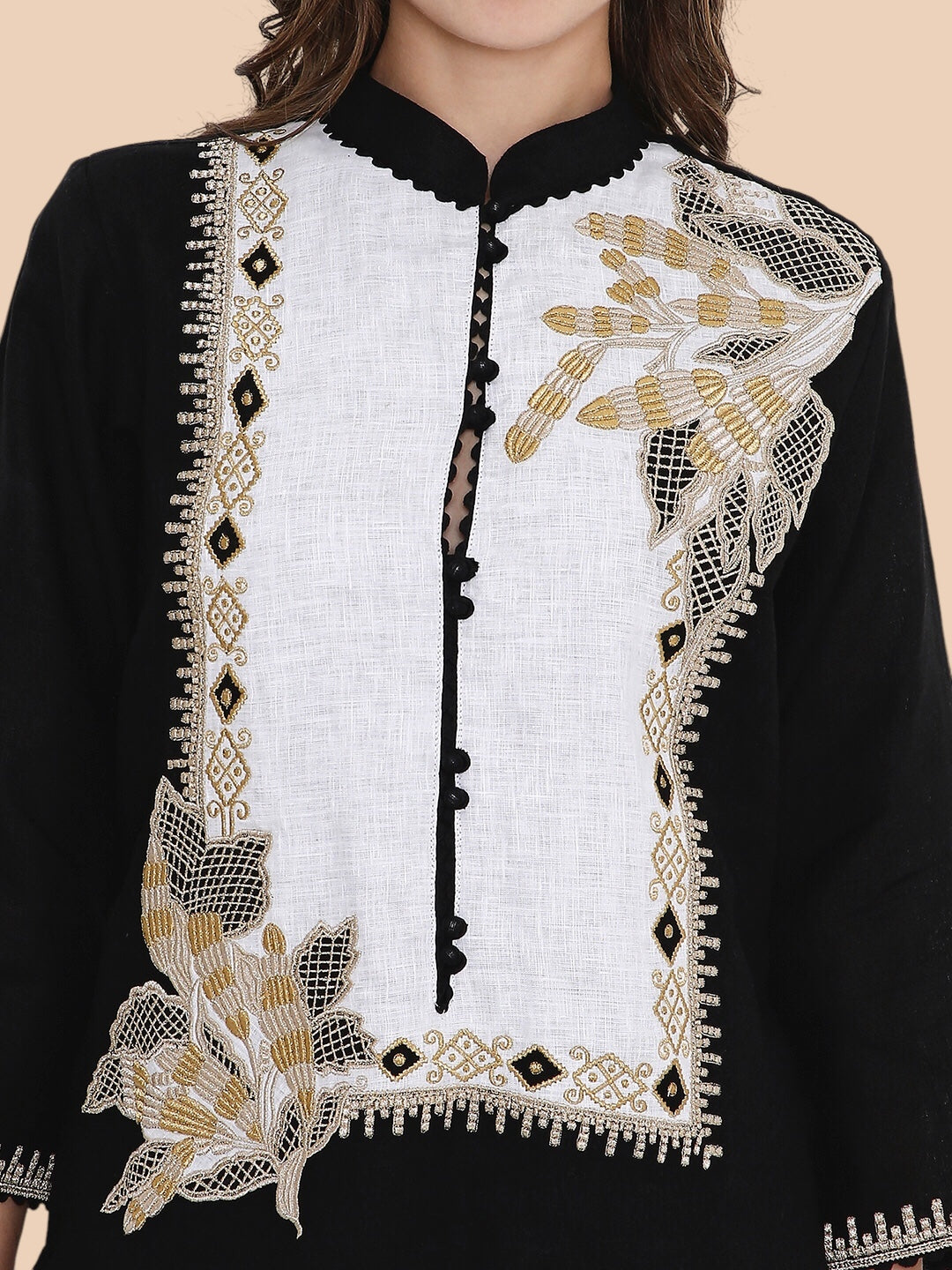Black and white embroidered garment with gold details on a beige background