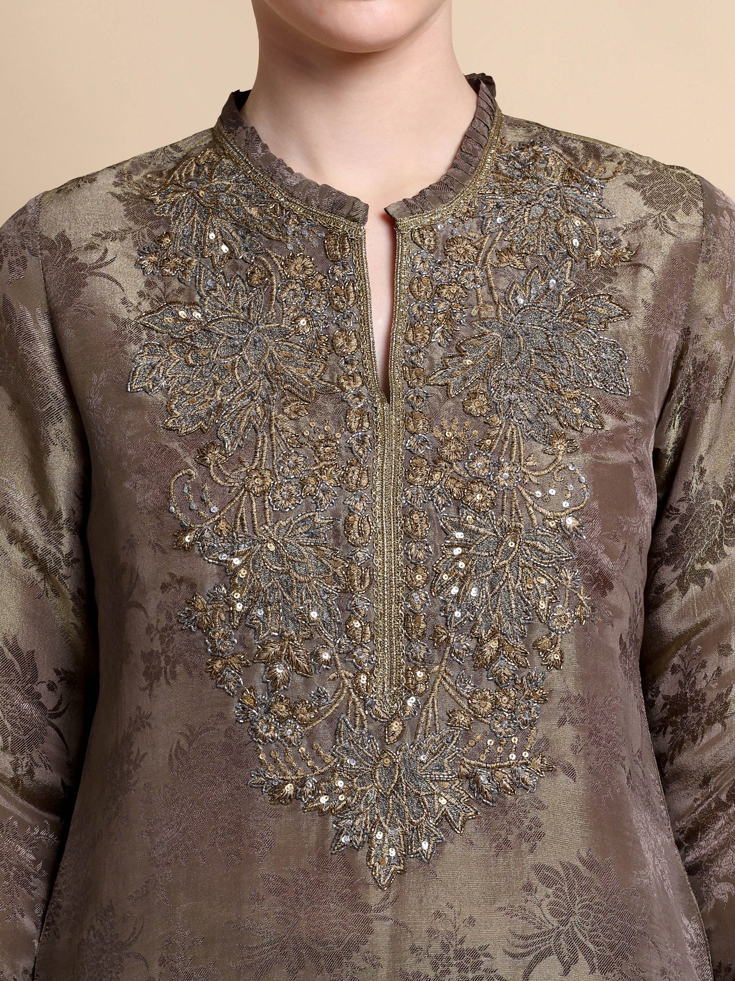 Brown embroidered garment with intricate patterns on a beige background