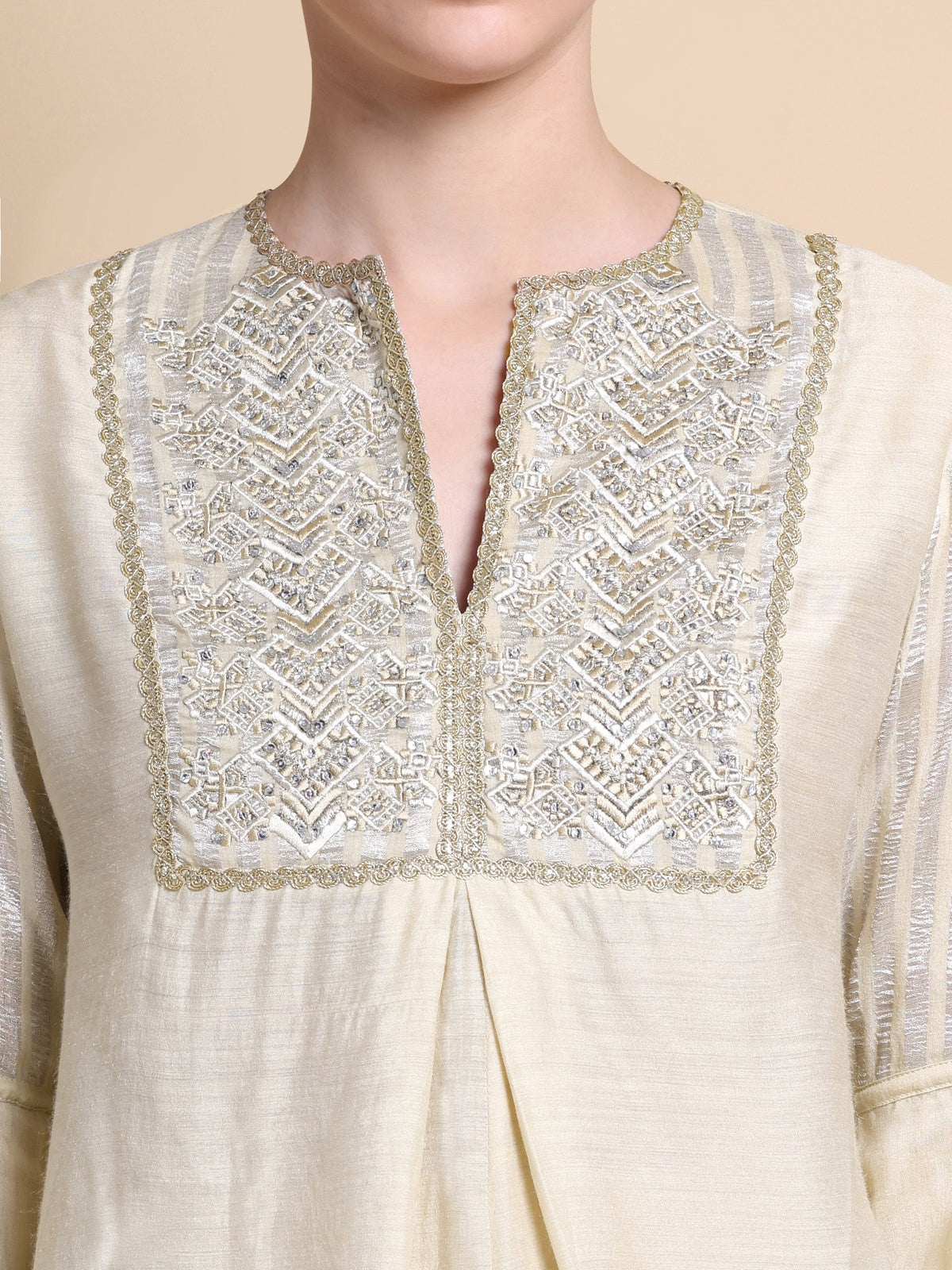 Close-up of a cream-colored kurta with intricate gold embroidery on a beige background