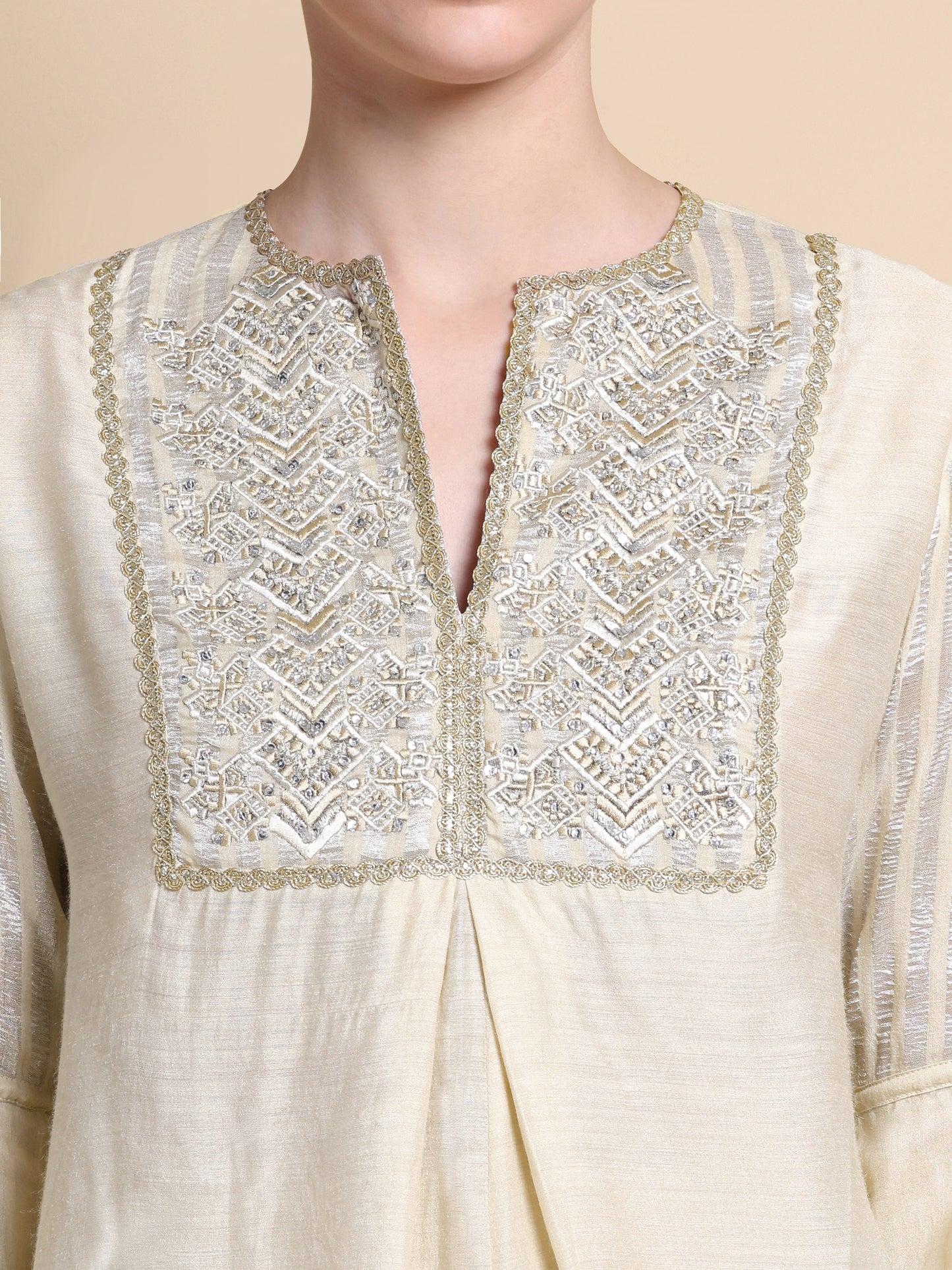 Close-up of a cream-colored kurta with intricate gold embroidery on a beige background