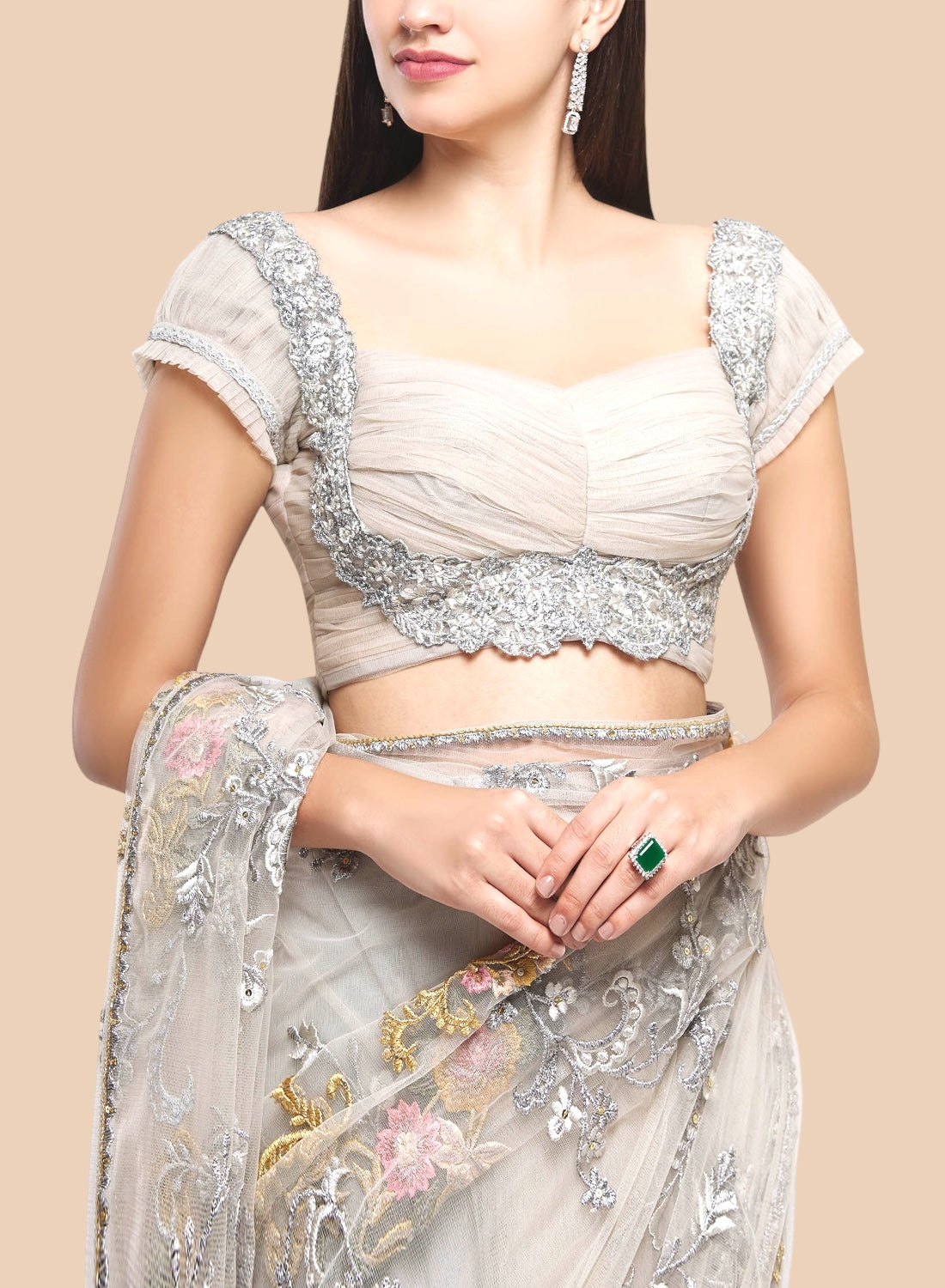 Woman wearing a silver and beige embroidered saree against a beige background