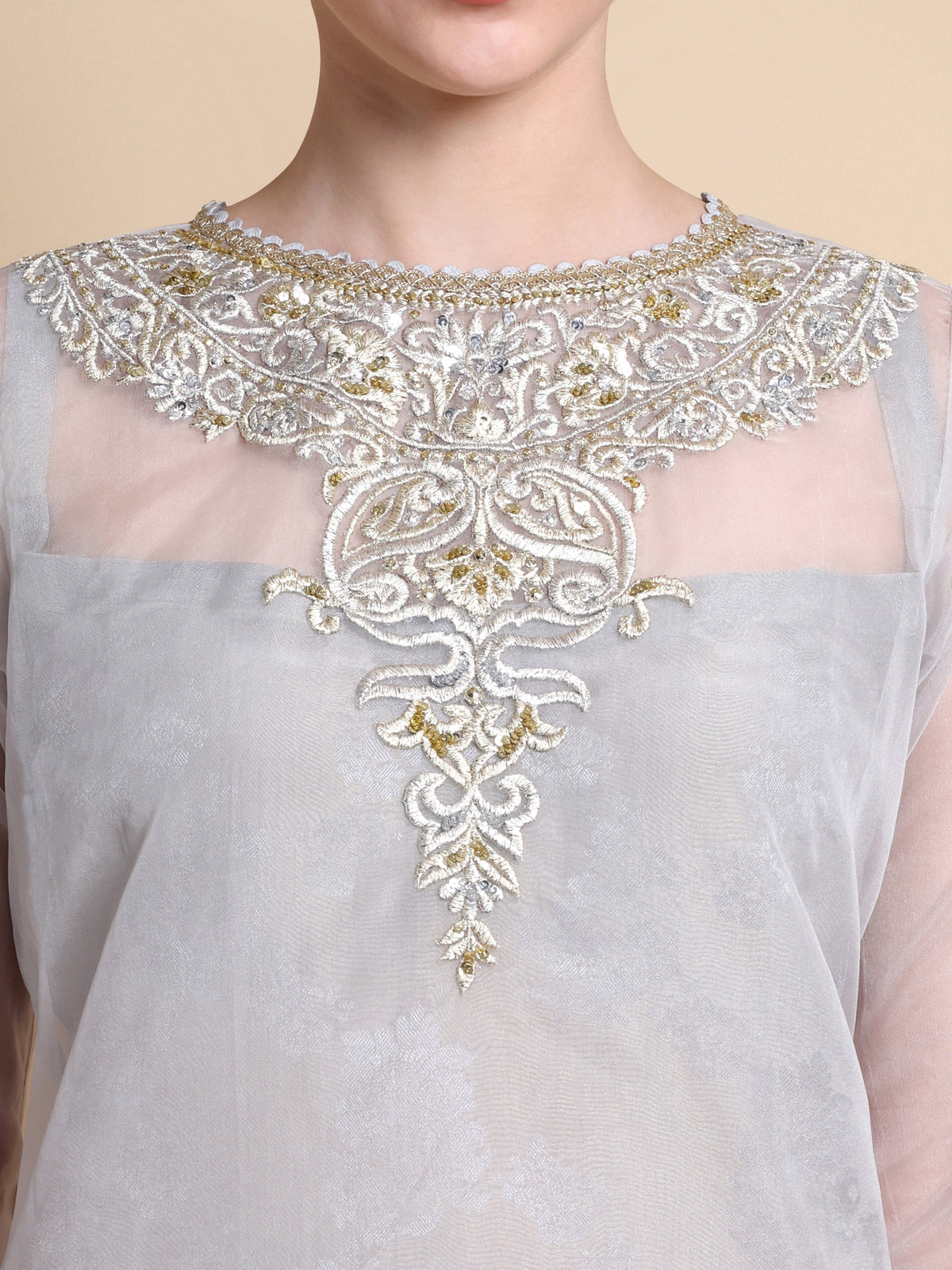 Gray top with intricate gold and white embroidery on a beige background