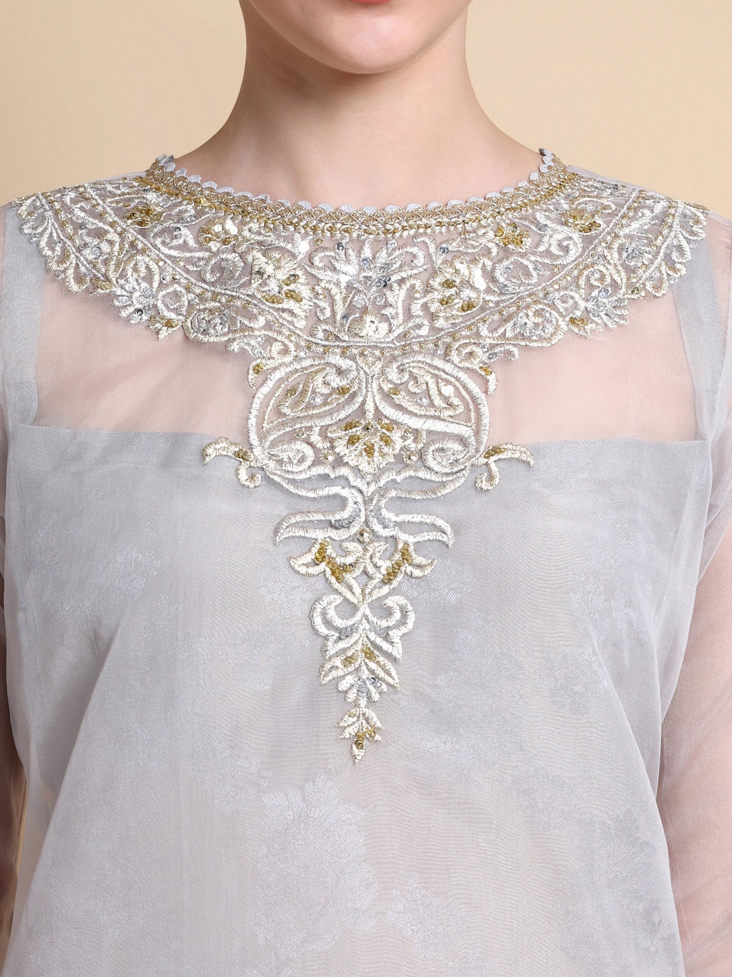 Gray top with intricate gold and white embroidery on a beige background