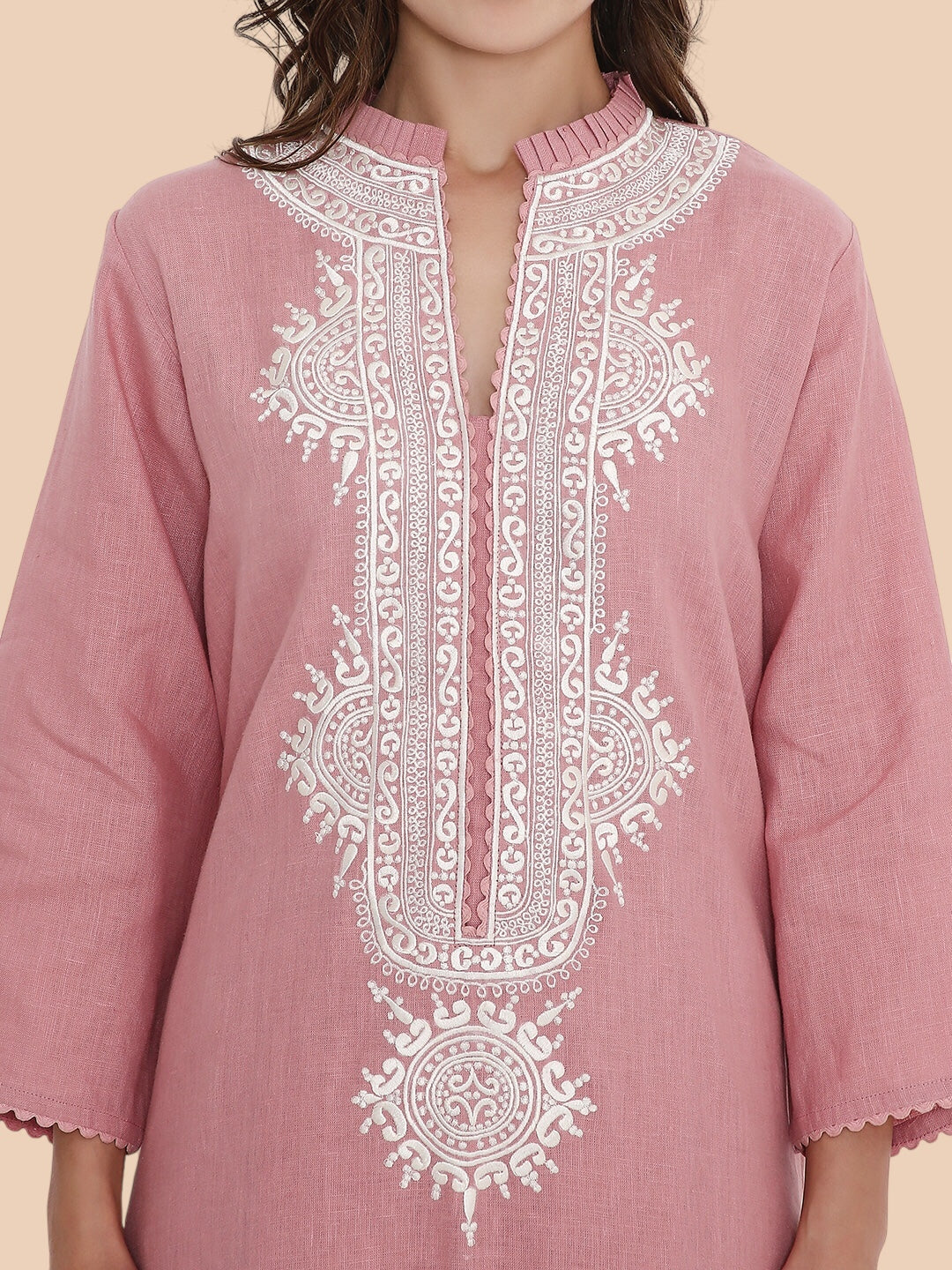 Pink embroidered dress with white patterns on a beige background
