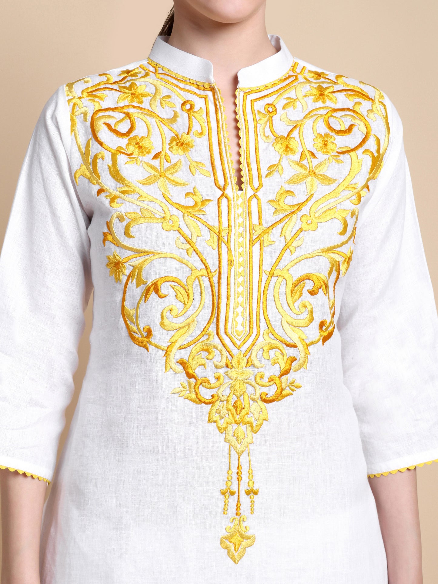 White top with intricate gold embroidery on a beige background