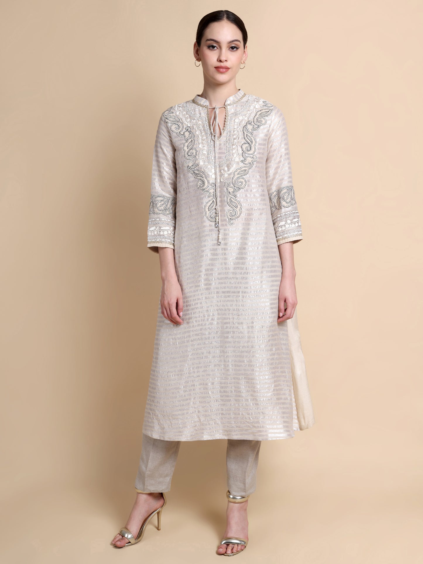 Woman wearing a white embroidered kurta with beige pants on a beige background