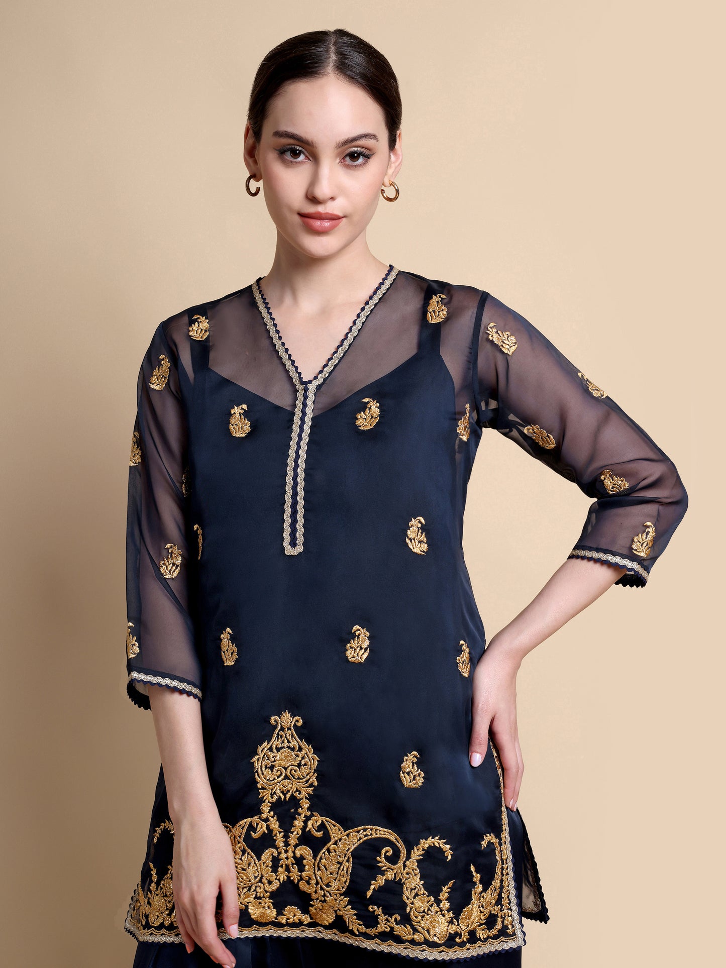 Woman wearing a navy blue dress with gold embroidery on a beige background