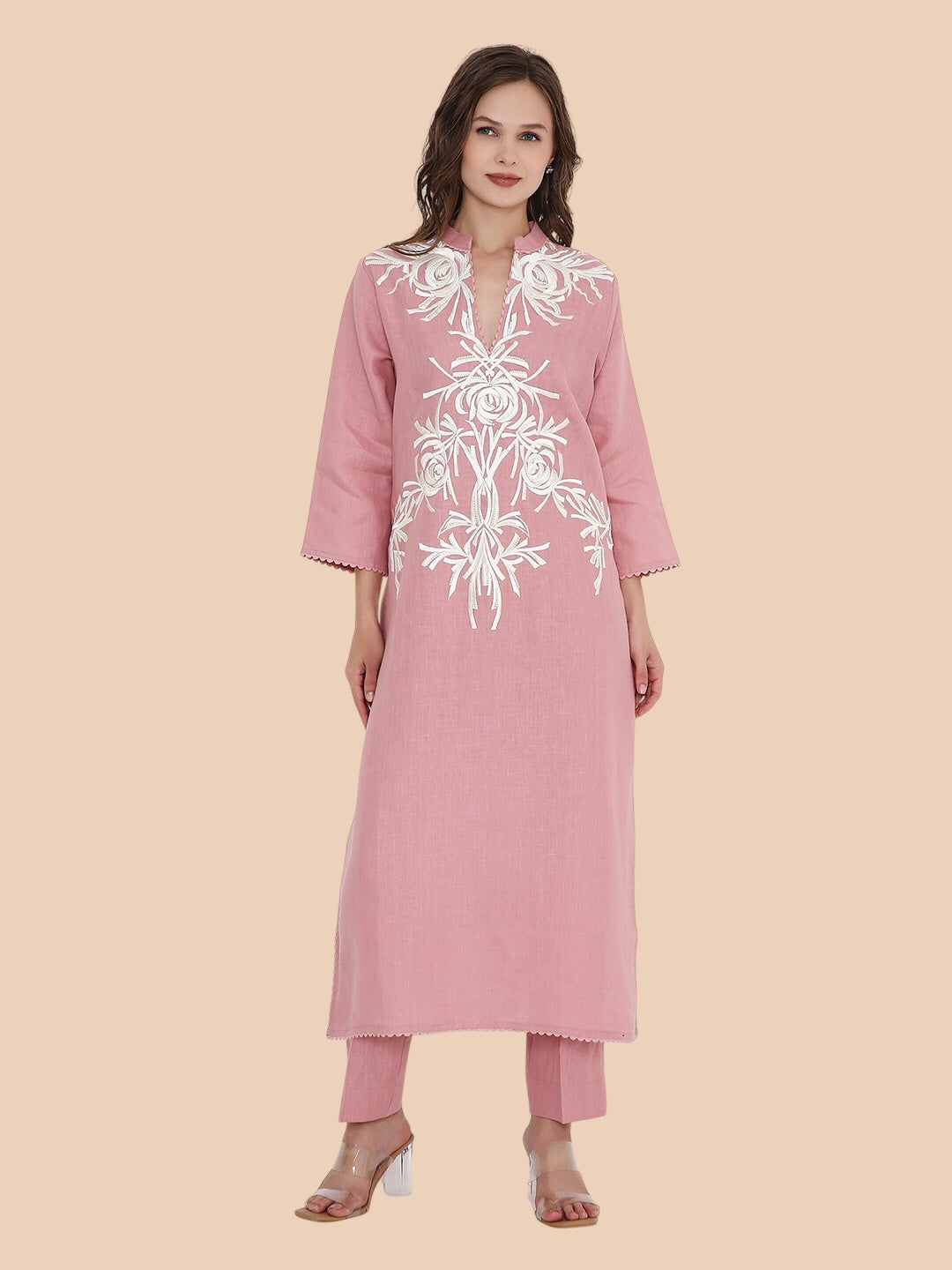 Woman wearing a pink kurta with white floral embroidery on a beige background