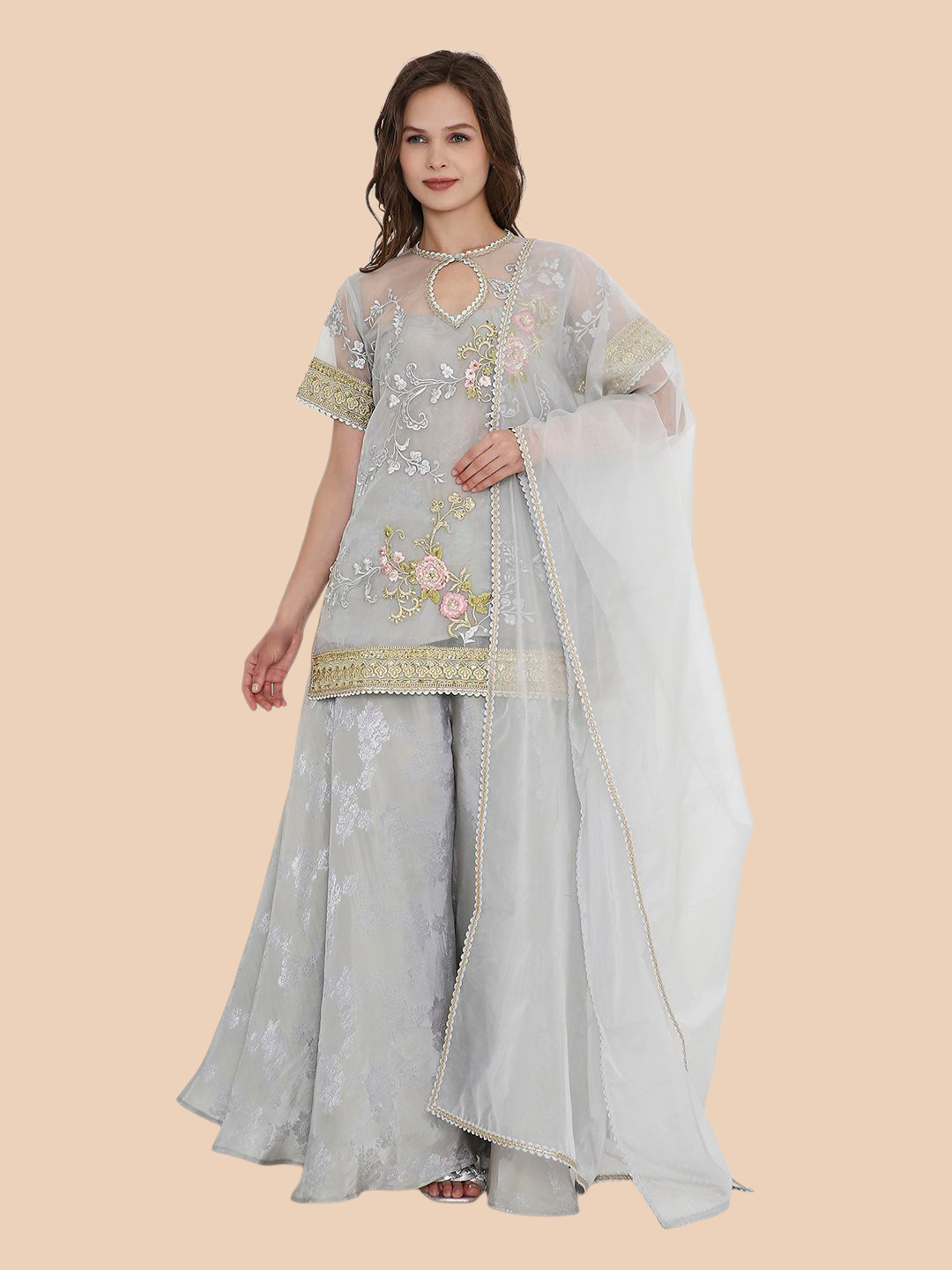 Woman wearing a light gray traditional outfit with floral embroidery on a beige background