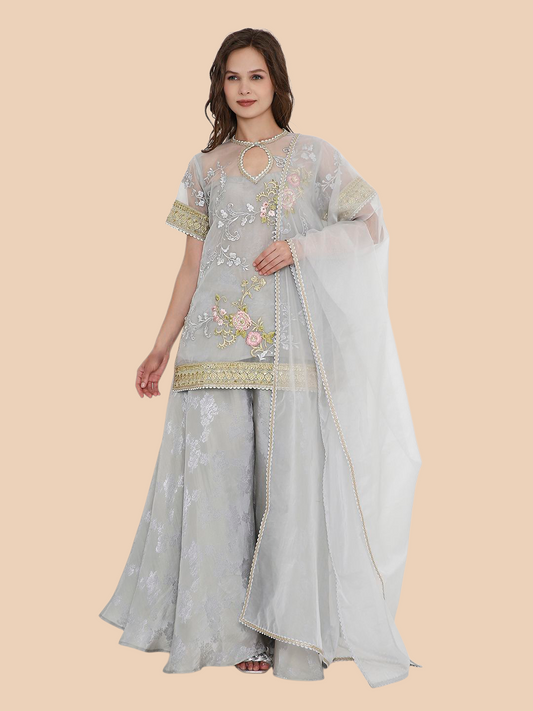 Woman wearing a light gray traditional outfit with floral embroidery on a beige background
