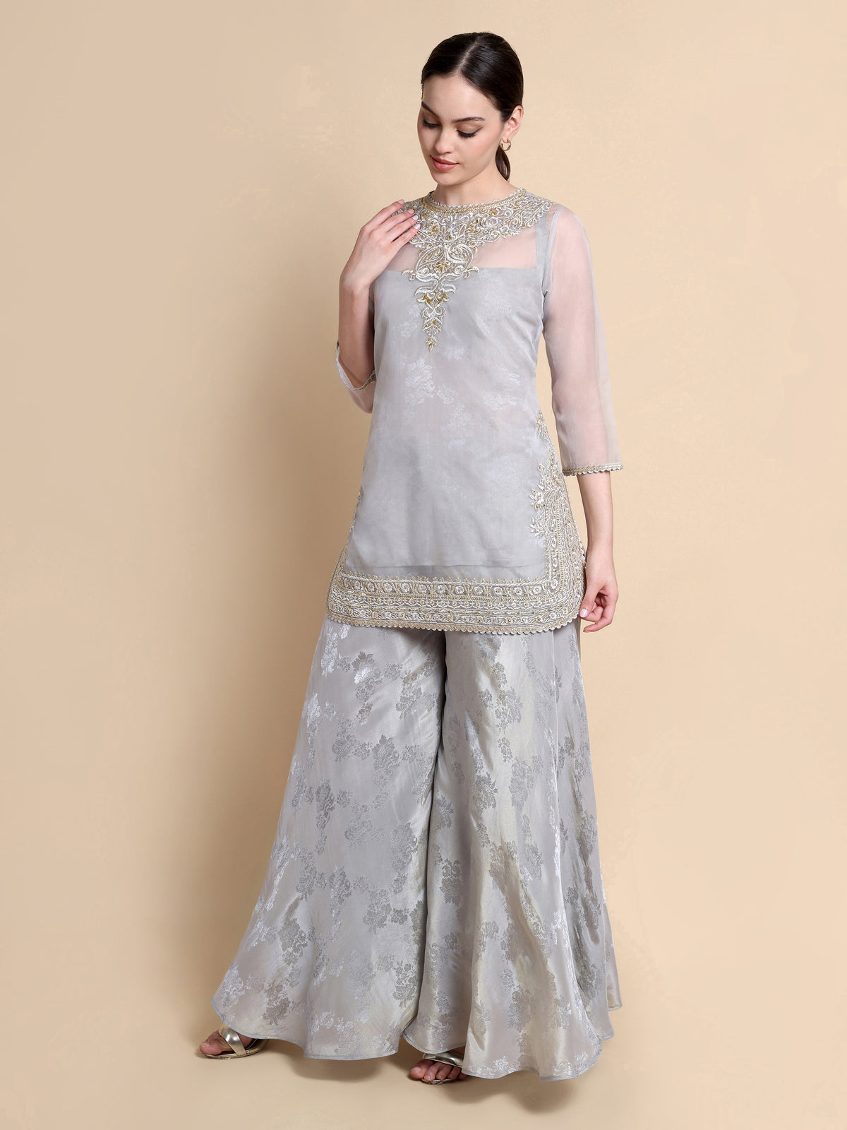 Woman wearing a light gray traditional outfit with intricate designs on a beige background