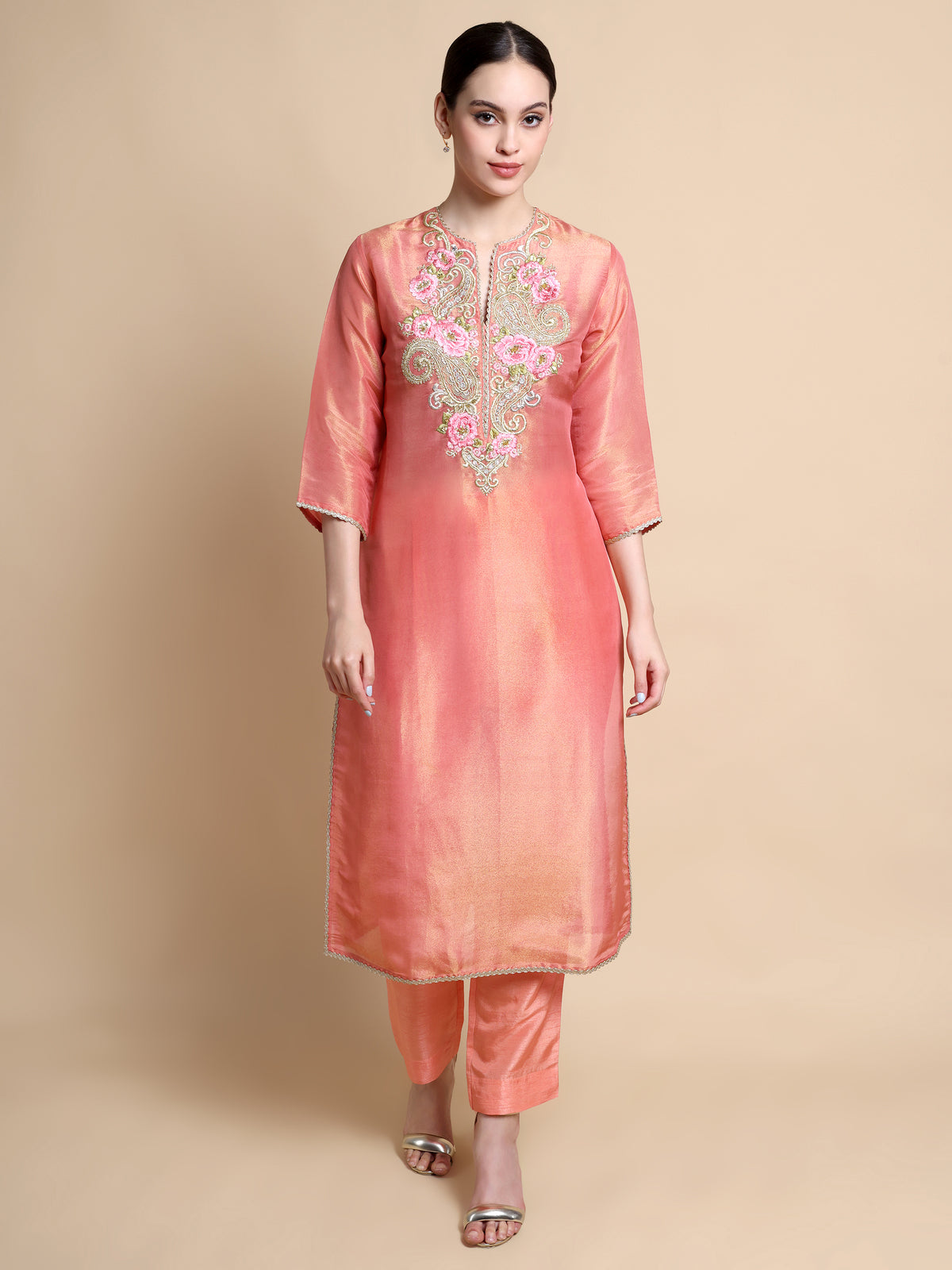 Woman wearing a peach kurta with floral embroidery on a beige background