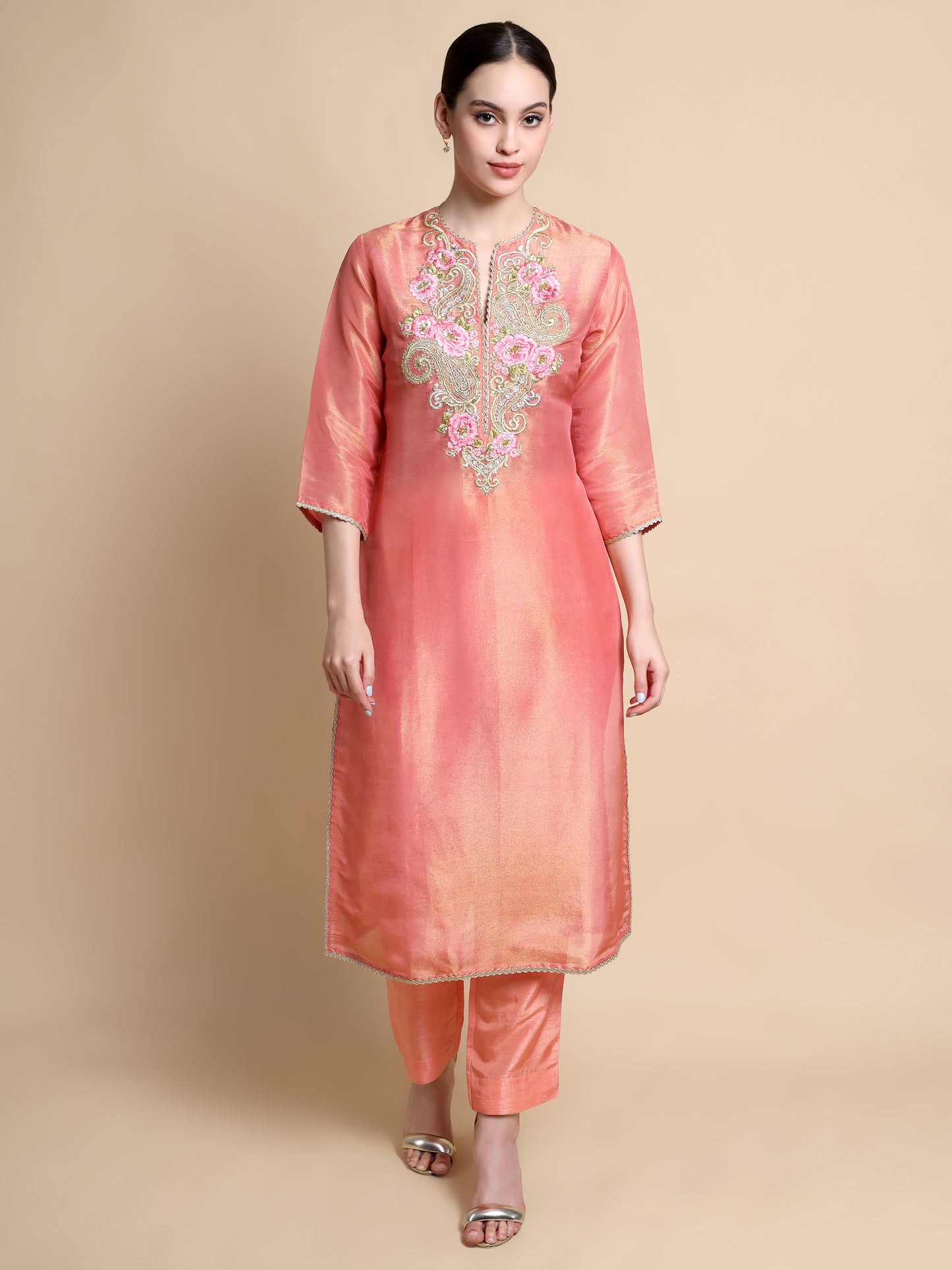 Woman wearing a peach kurta with floral embroidery on a beige background