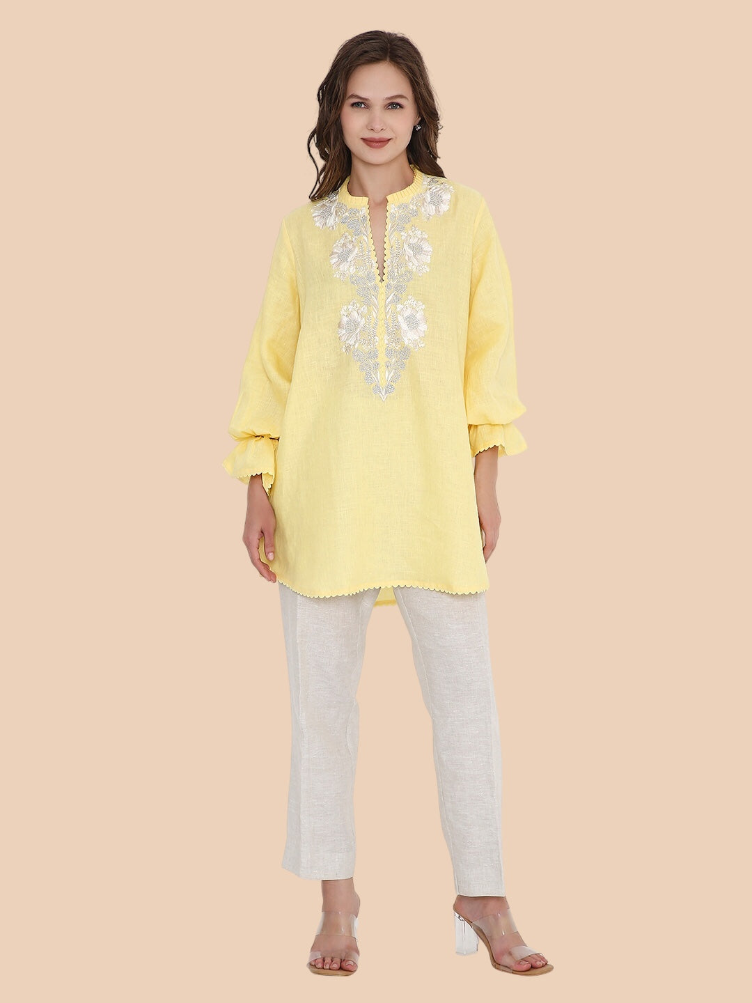 Woman wearing a yellow embroidered top and white pants on a beige background