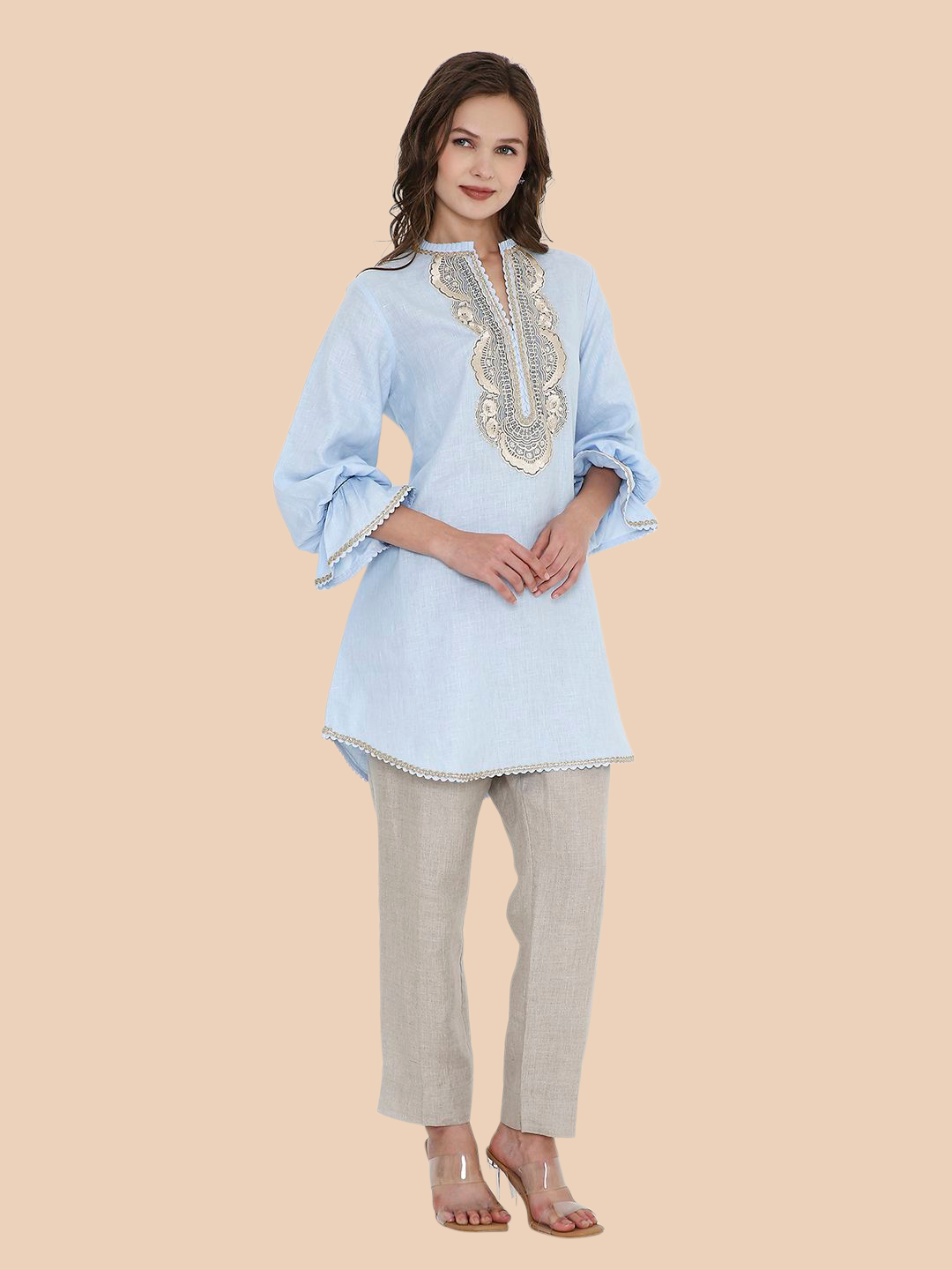 Woman wearing a light blue embroidered top and gray pants on a beige background