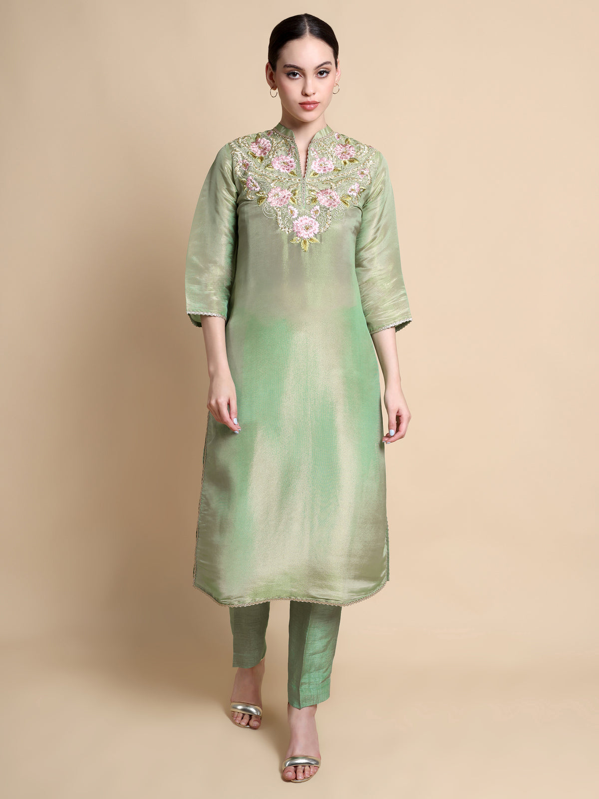 Woman wearing a green embroidered kurta with pants on a beige background