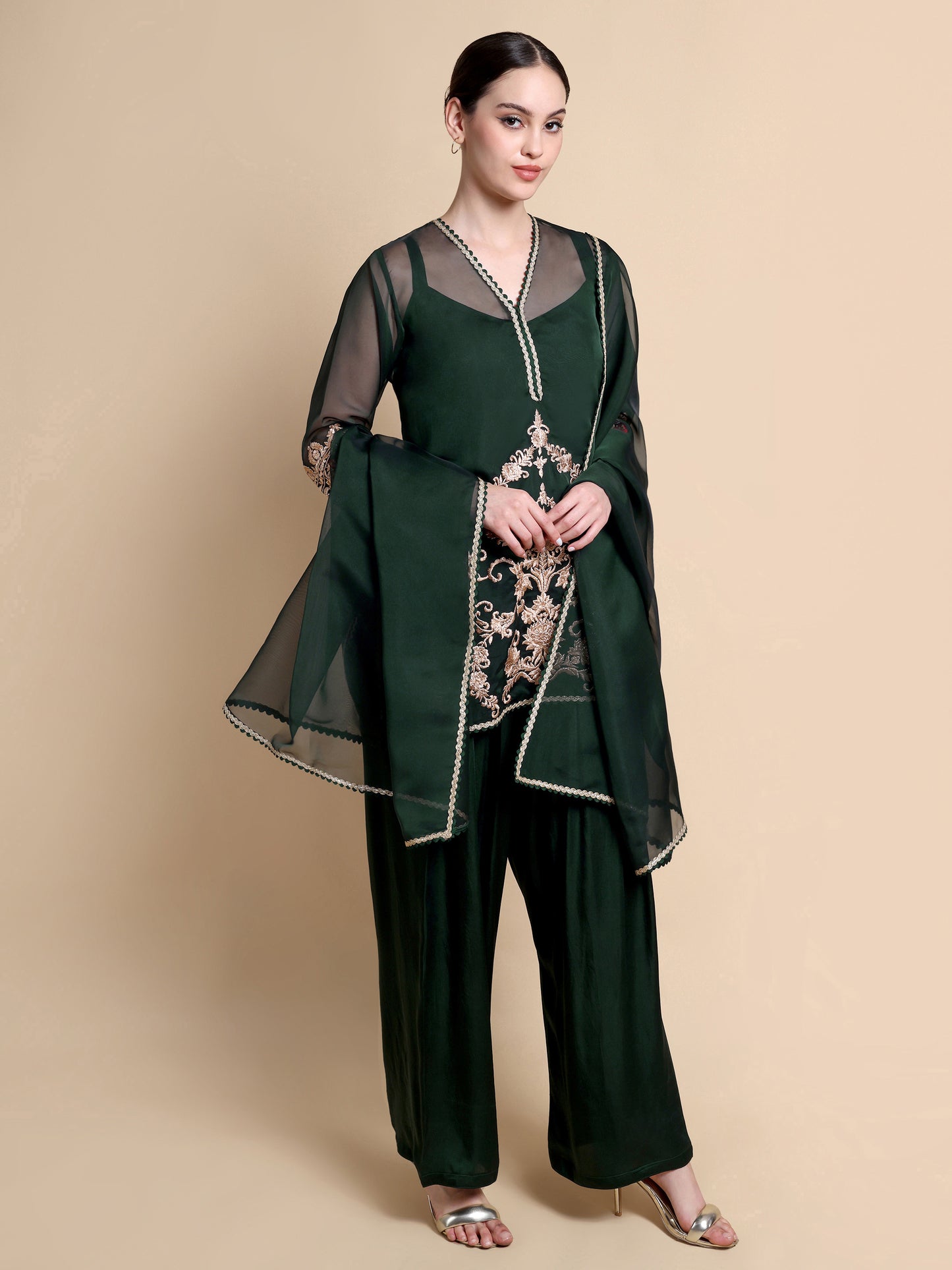 Woman wearing a dark green outfit with floral embroidery on a beige background