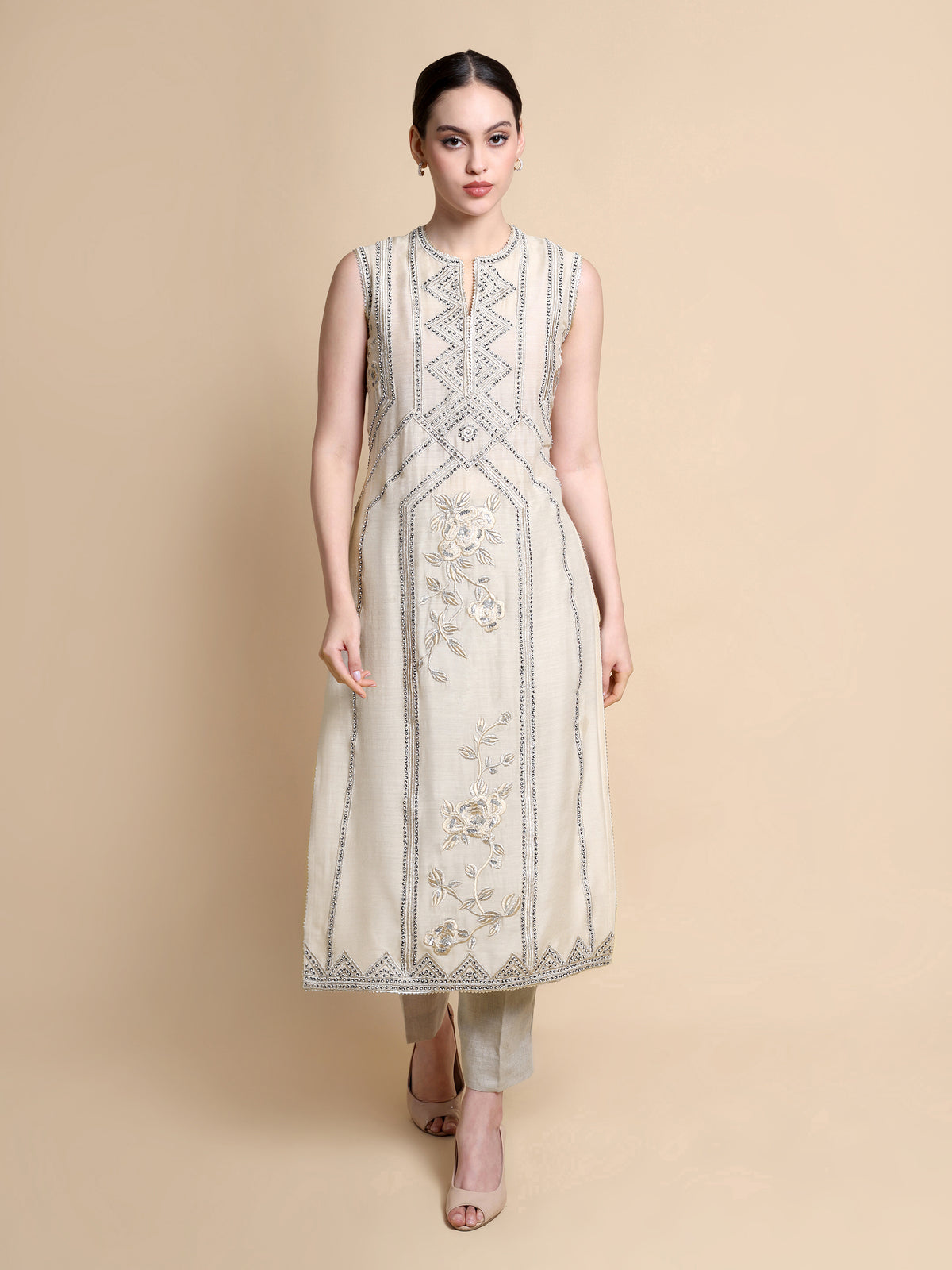 Woman wearing a beige sleeveless kurta with intricate patterns on a beige background