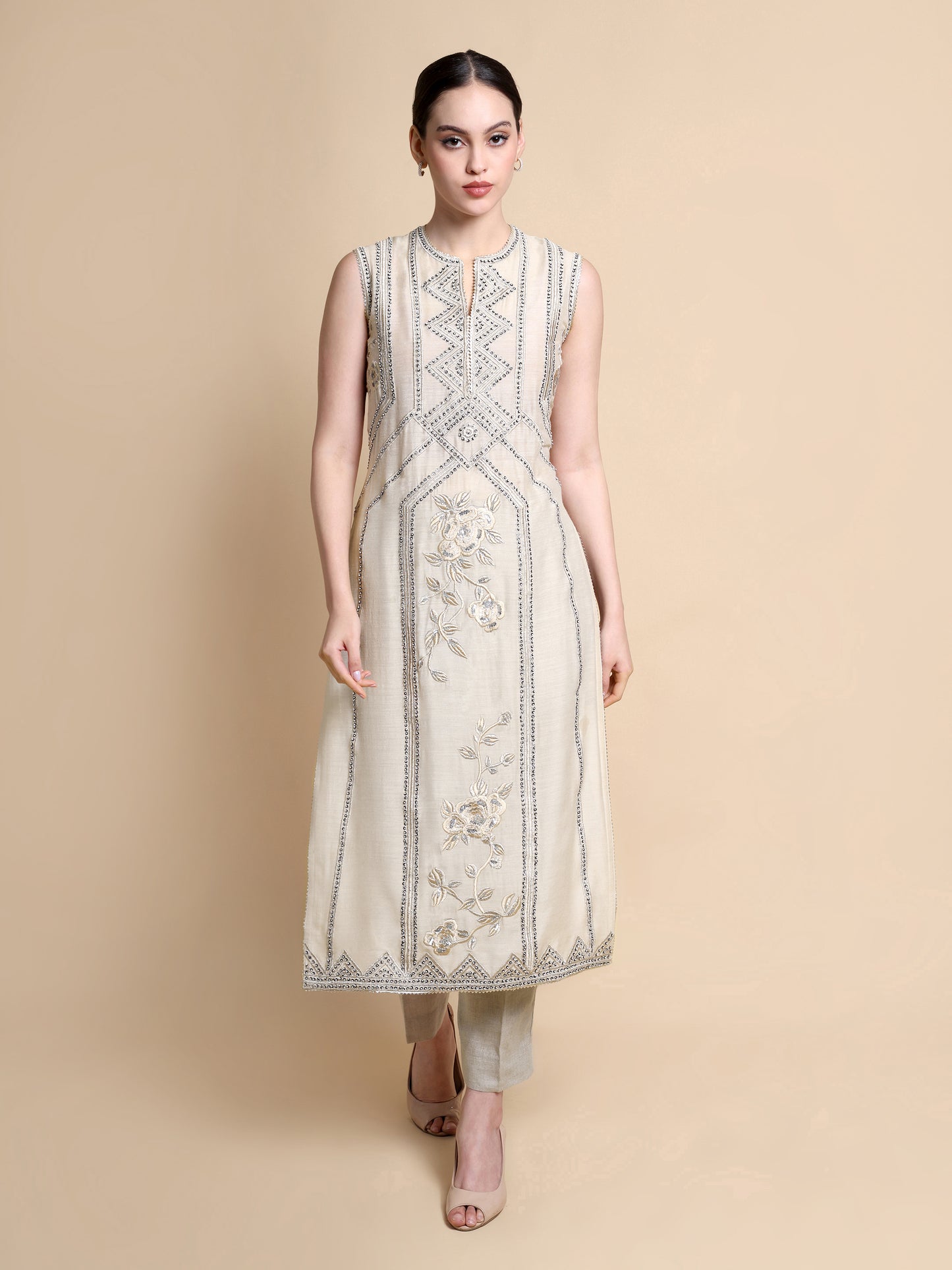 Woman wearing a beige sleeveless kurta with intricate patterns on a beige background