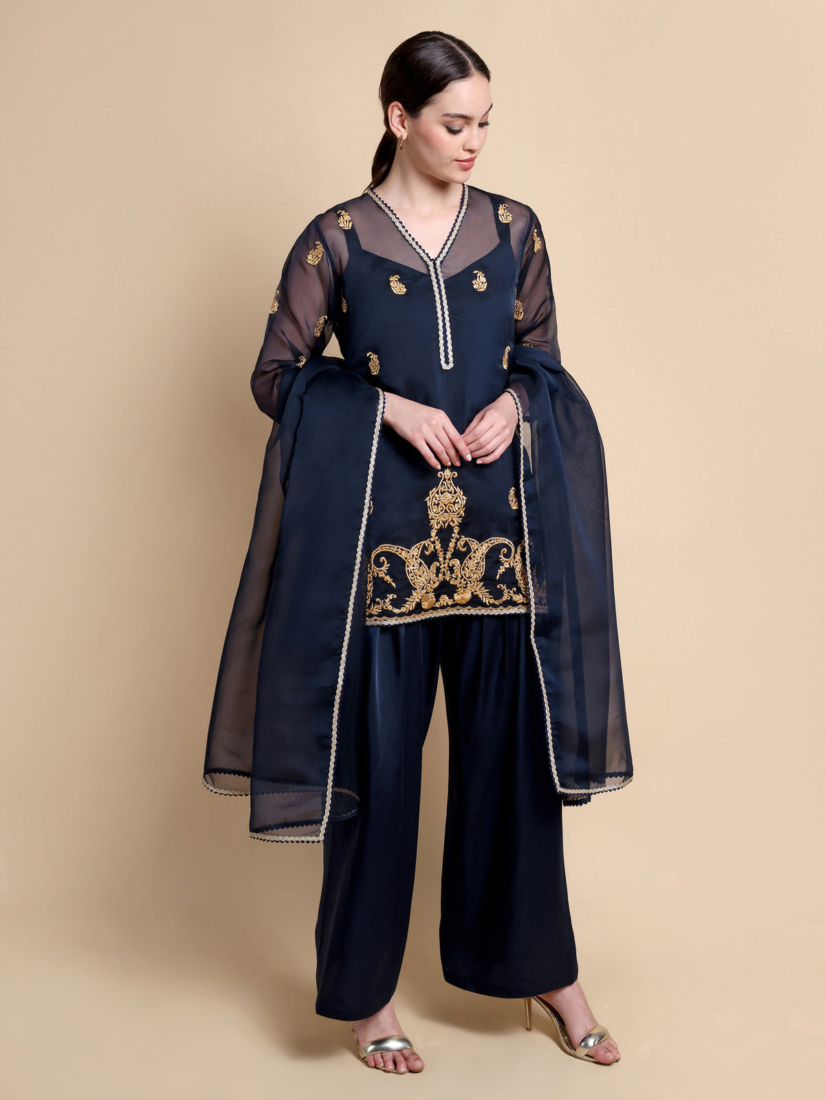 Woman wearing a navy blue traditional outfit with gold embroidery on a beige background