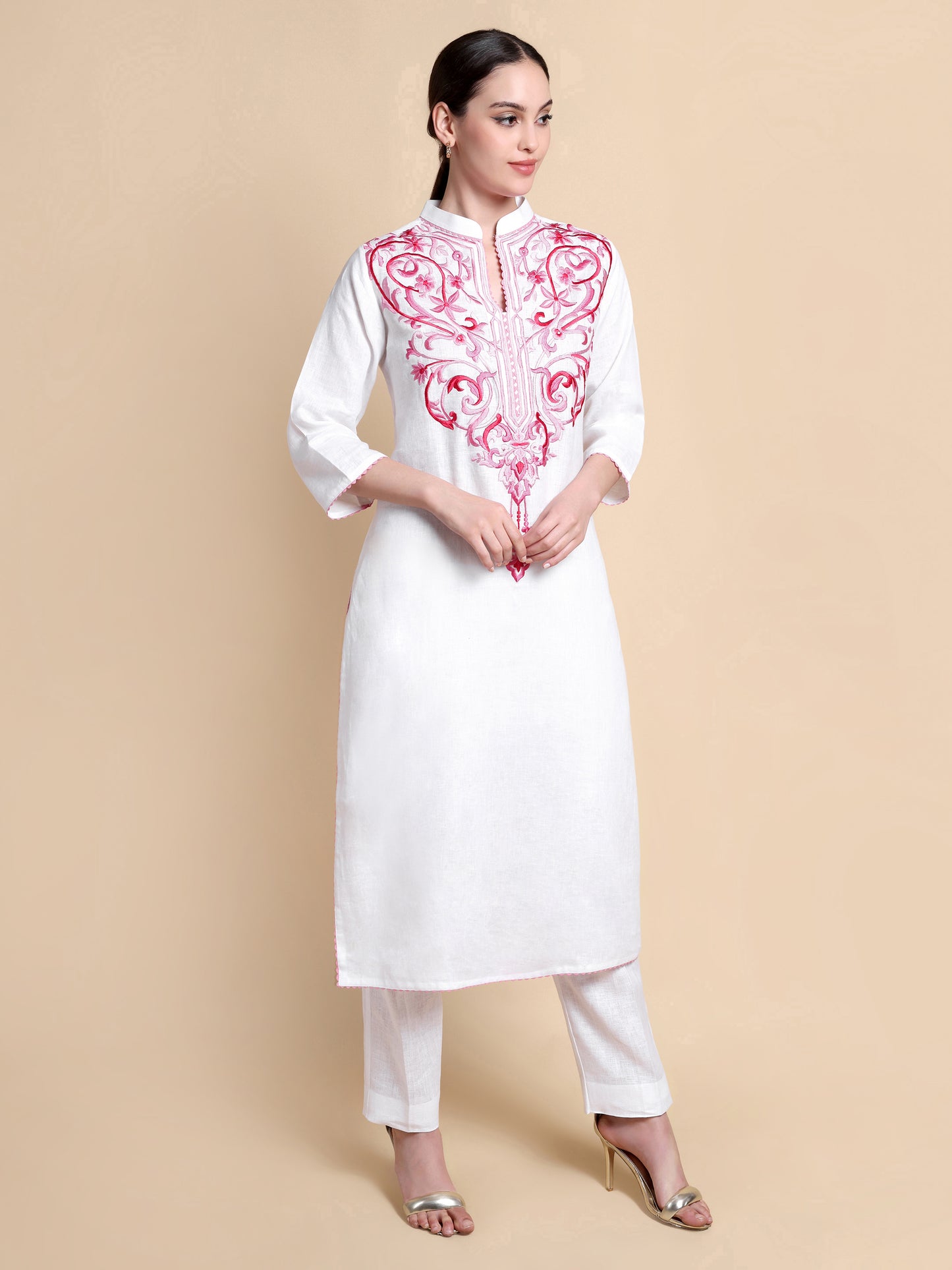 Woman wearing a white kurta with pink embroidery on a beige background