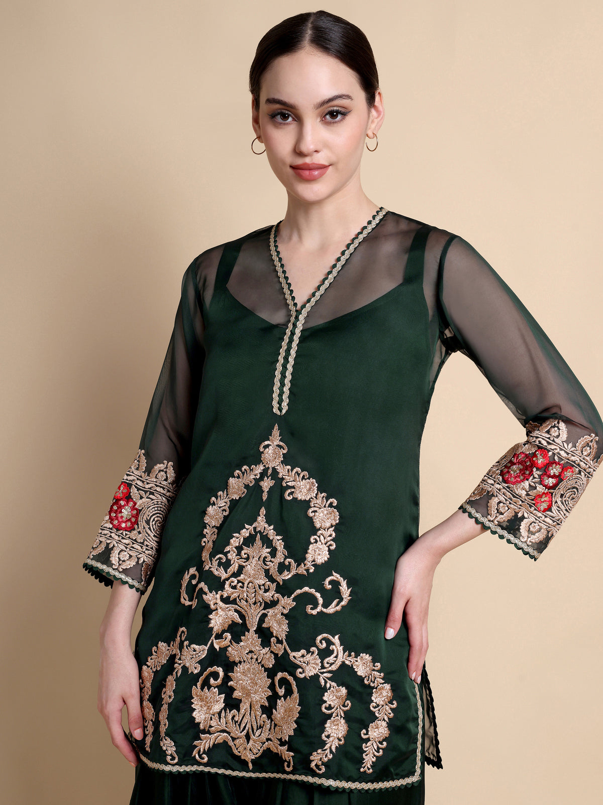 Woman wearing a dark green embroidered dress with sheer sleeves on a beige background