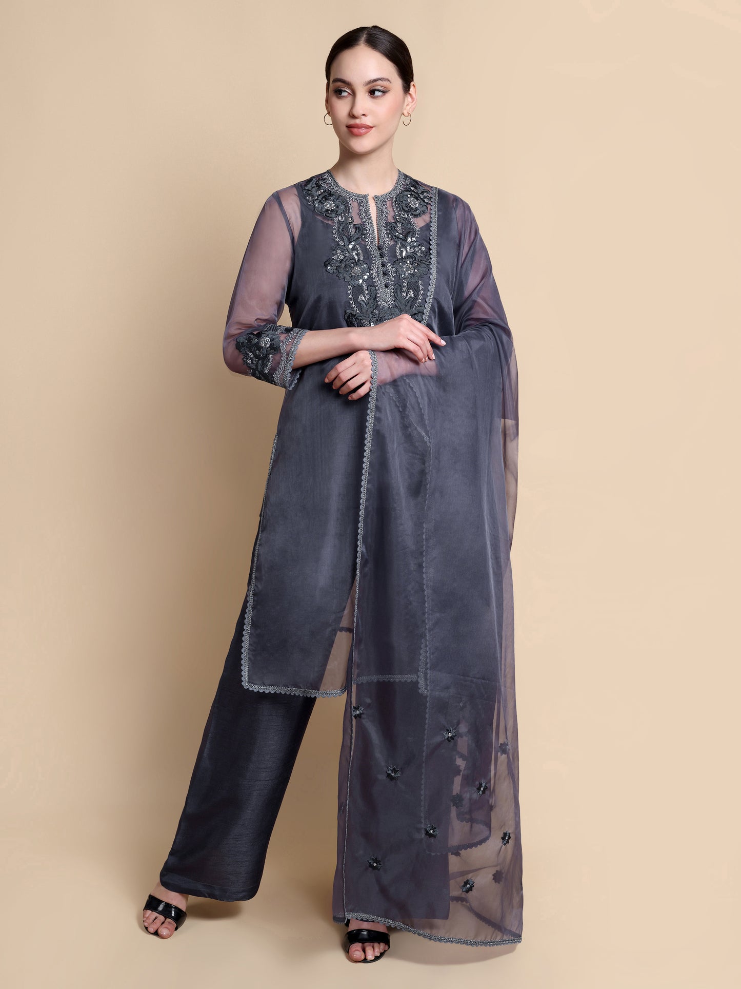 Woman wearing a dark gray traditional outfit with intricate designs on a beige background