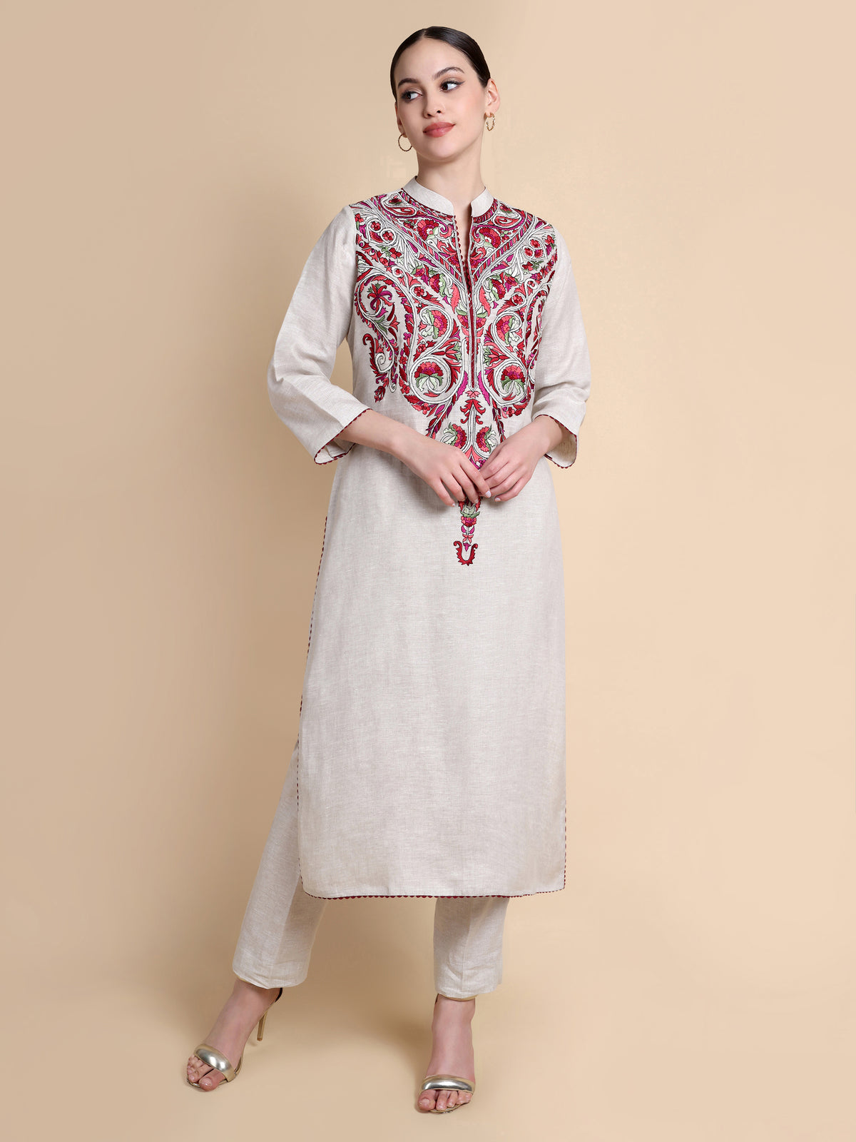 Woman wearing a white kurta with red and gold embroidery on a beige background
