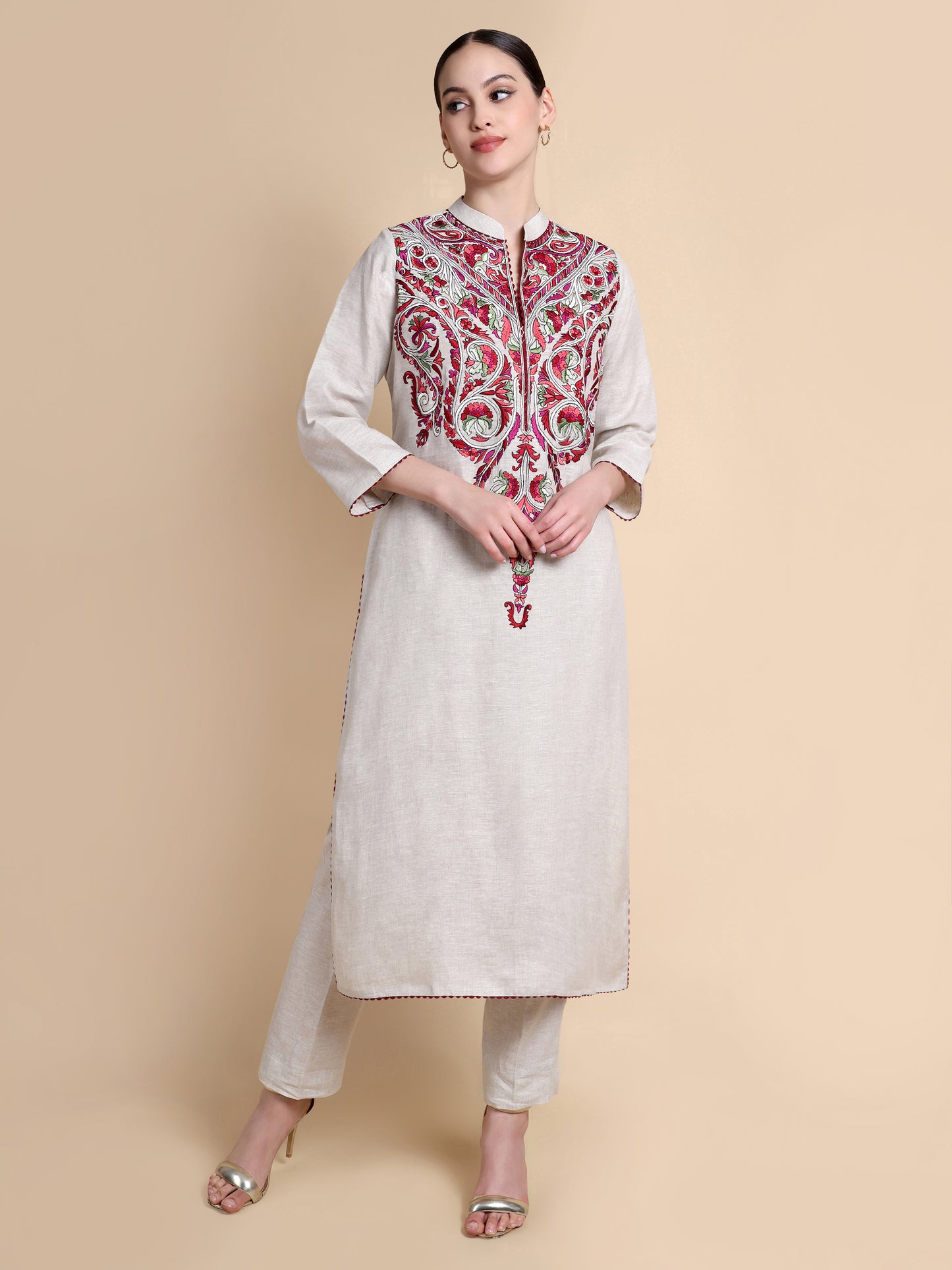 Woman wearing a white kurta with red and gold embroidery on a beige background