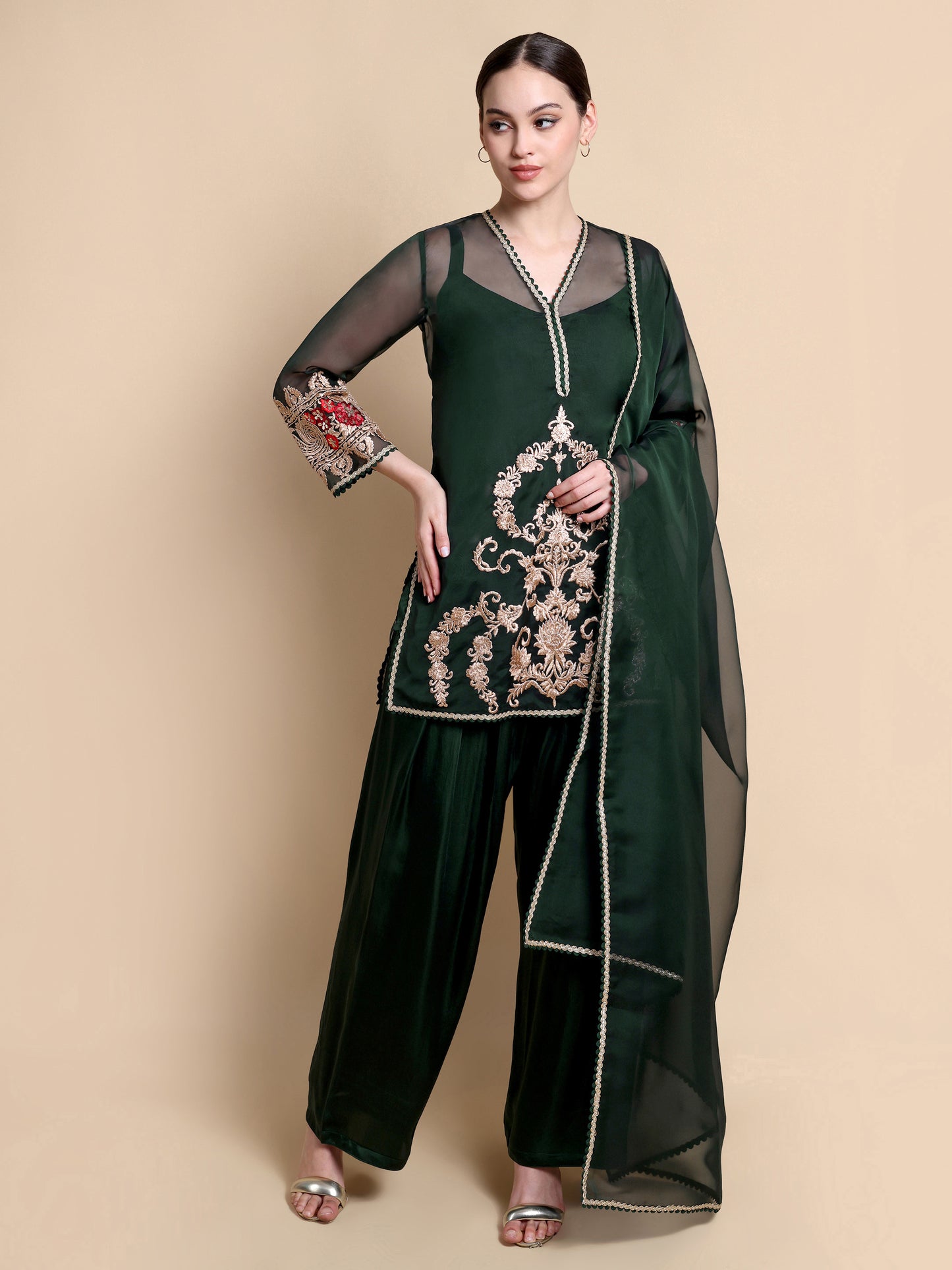 Woman wearing a dark green traditional outfit with embroidery on a beige background