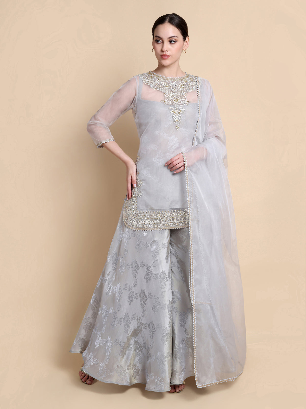 Woman wearing a light gray traditional outfit with embroidery on a beige background