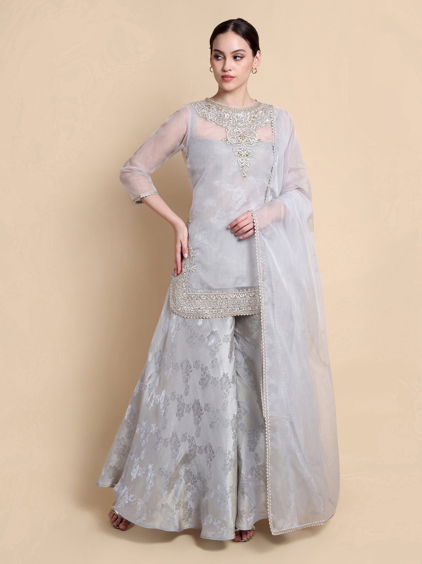 Woman wearing a light gray traditional outfit with embroidery on a beige background