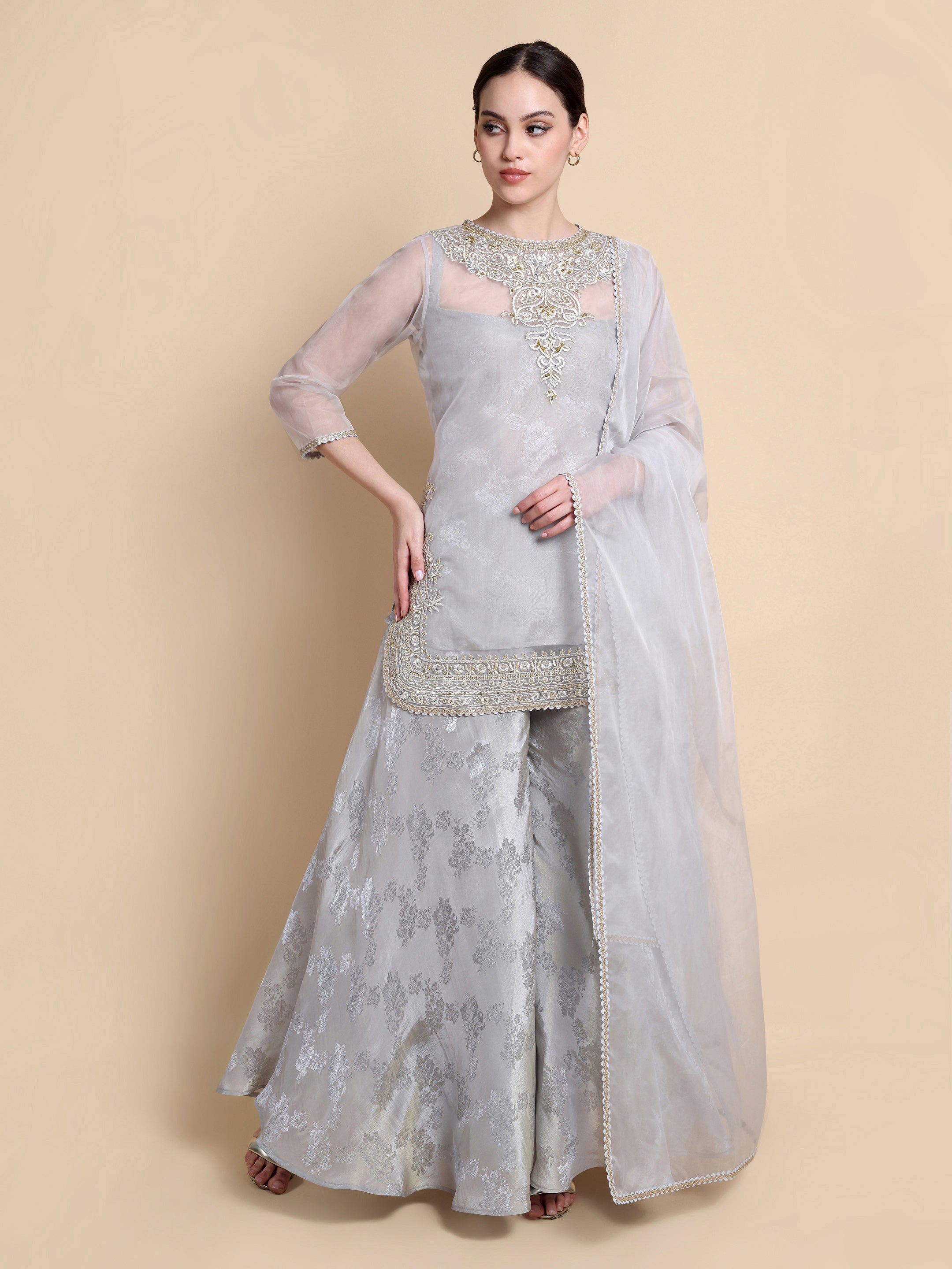 Woman wearing a light gray traditional outfit with embroidery on a beige background