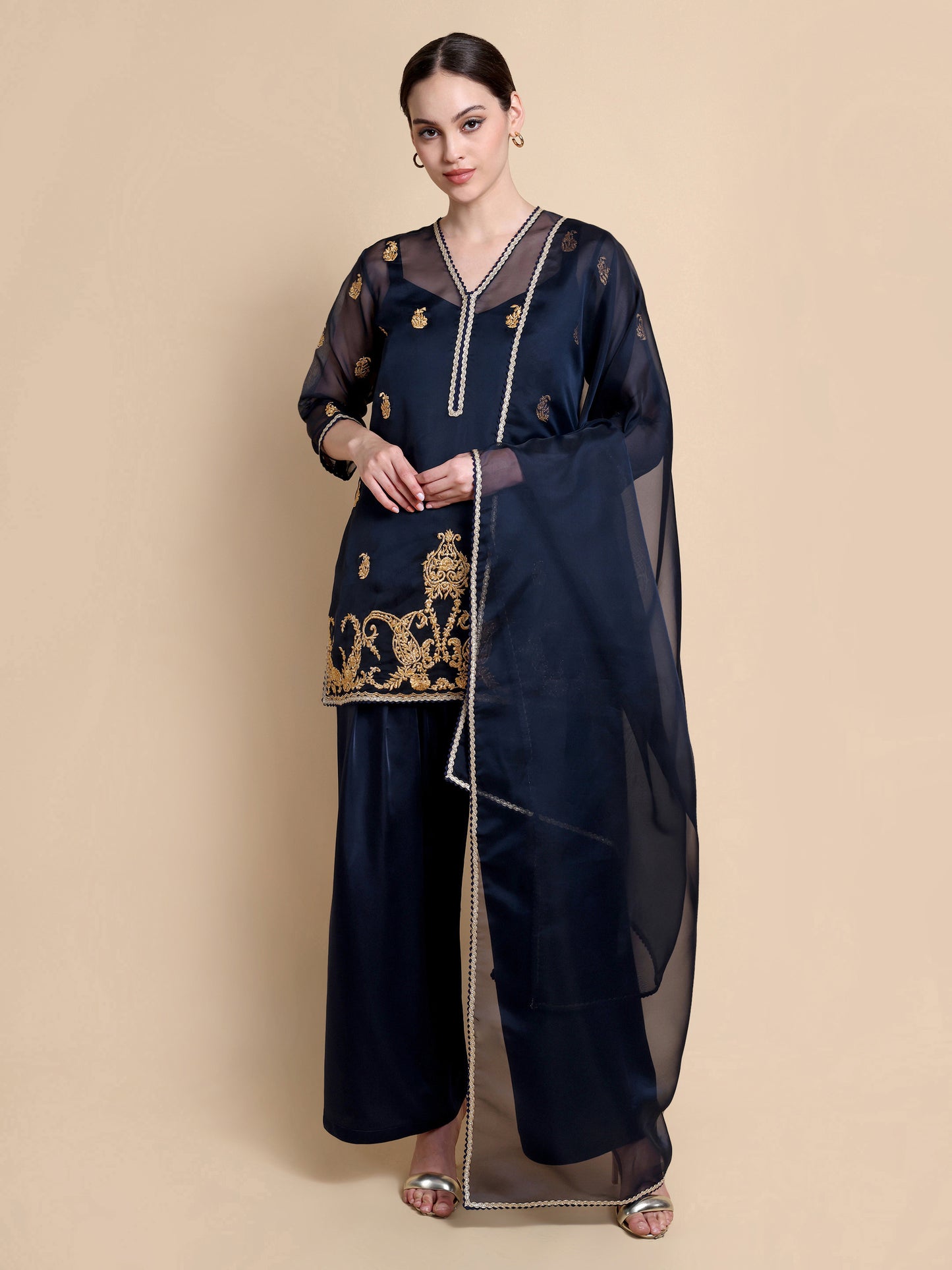 Woman wearing a navy blue traditional outfit with gold embroidery on a beige background