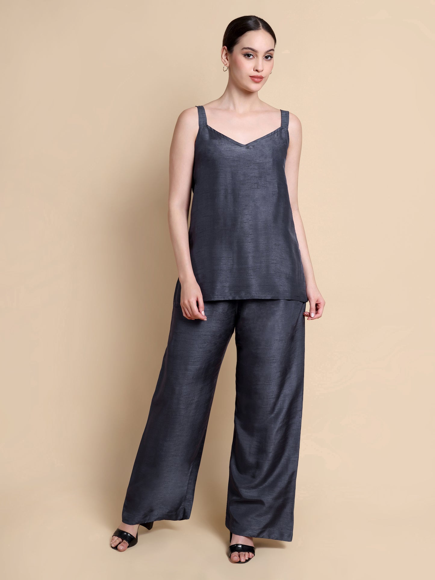 Woman wearing a dark gray sleeveless top and wide-leg pants on a beige background